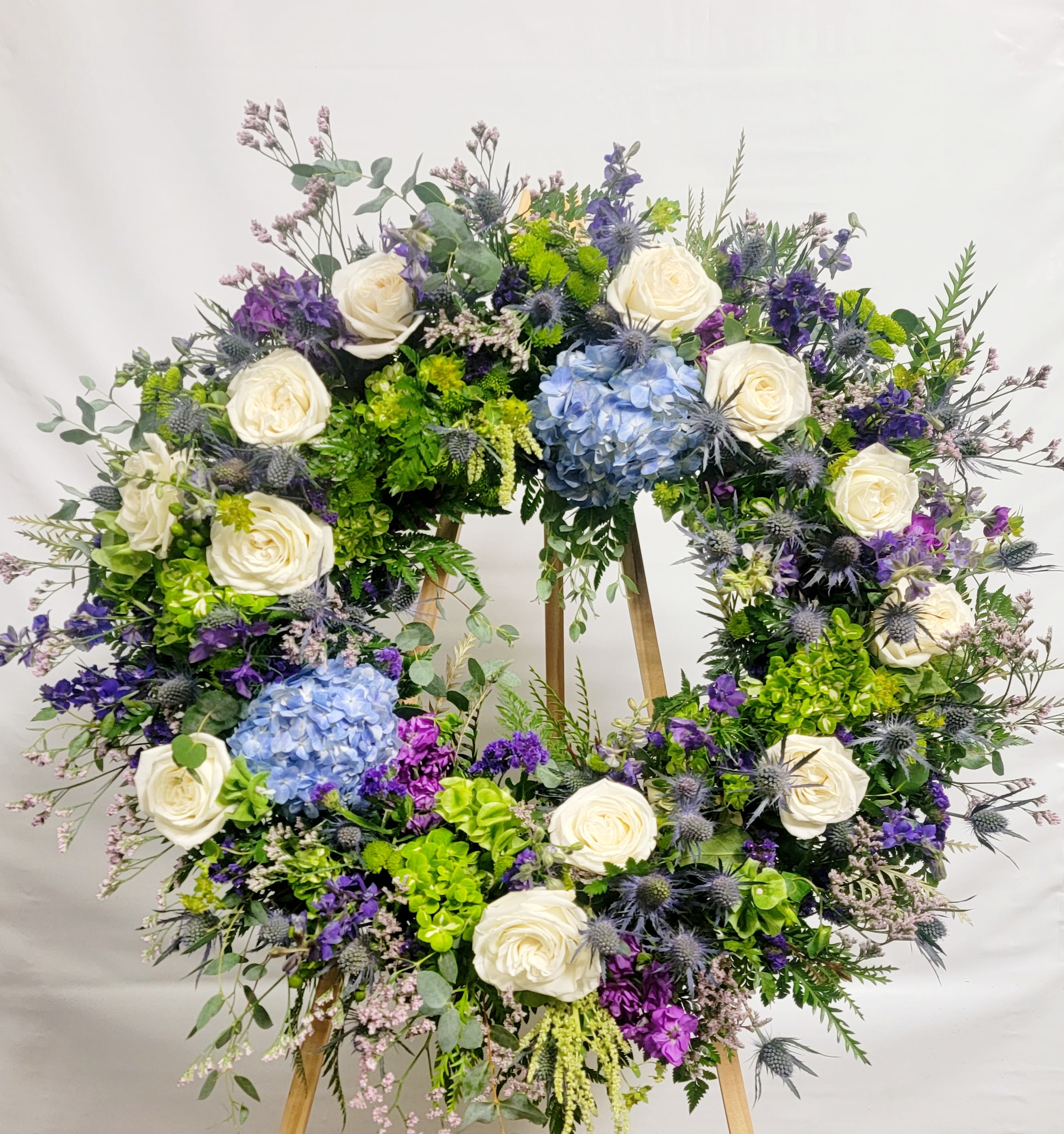 Large floral wreath with white roses, blue hydrangeas, and purple flowers