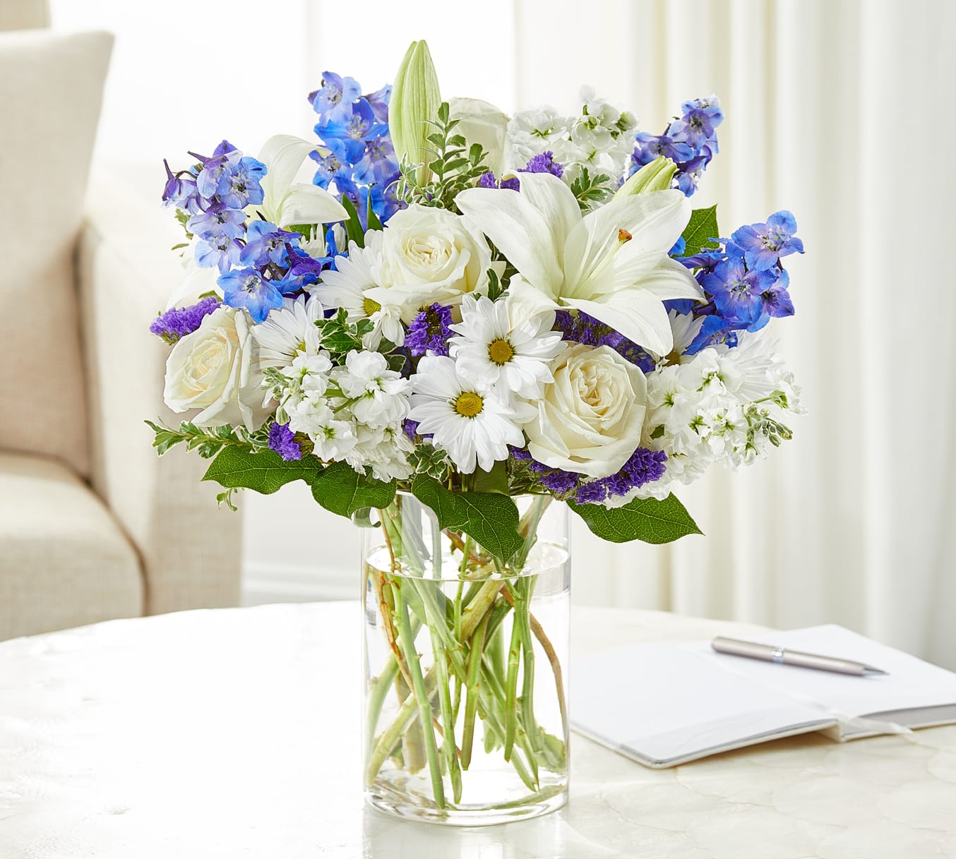 White roses and lilies with blue flowers in a clear glass vase