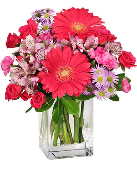Pink gerbera daisies, roses, and purple daisies in a clear glass vase
