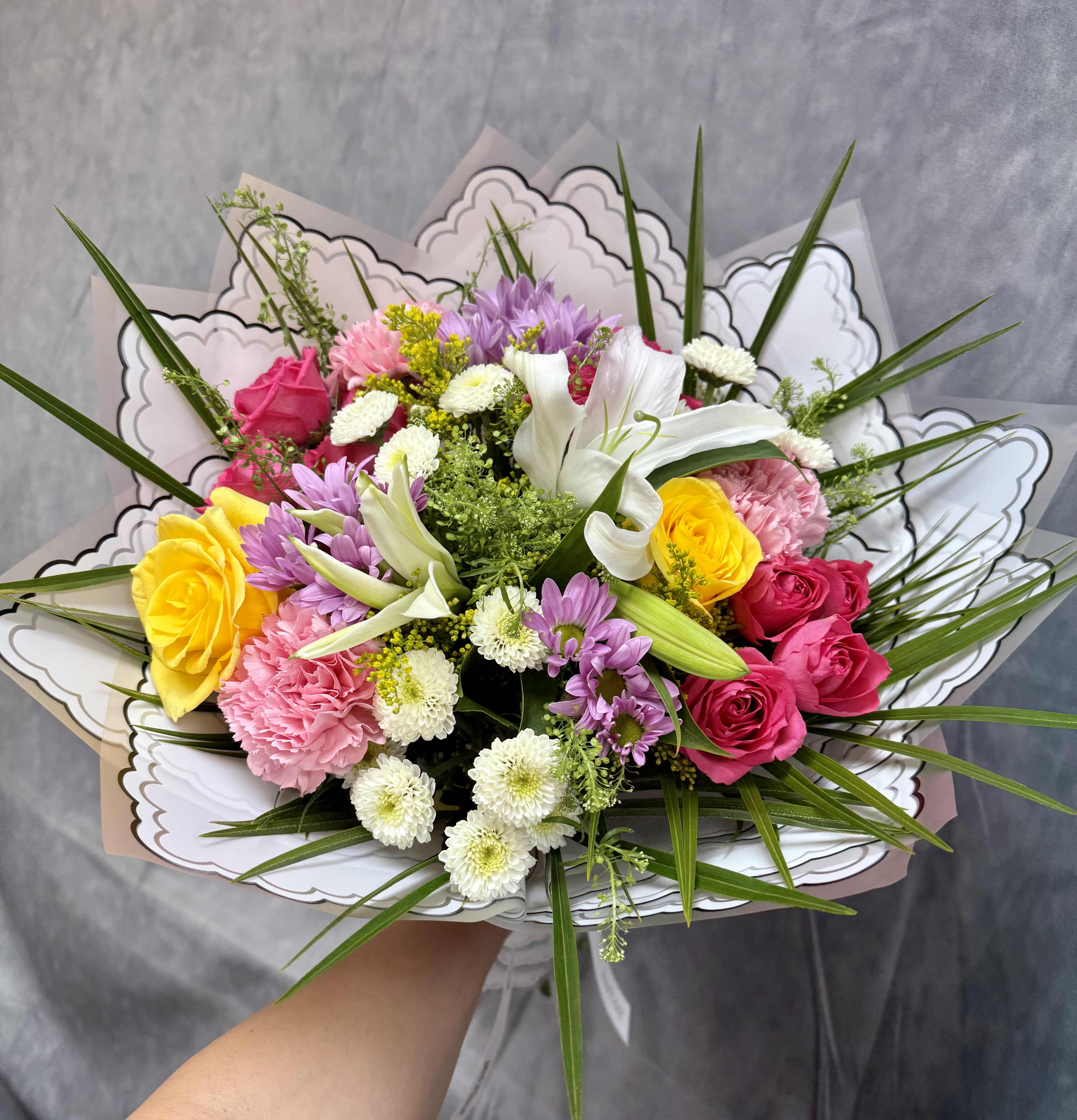 Mixed bouquet of roses, lilies, and daisies in decorative wrap