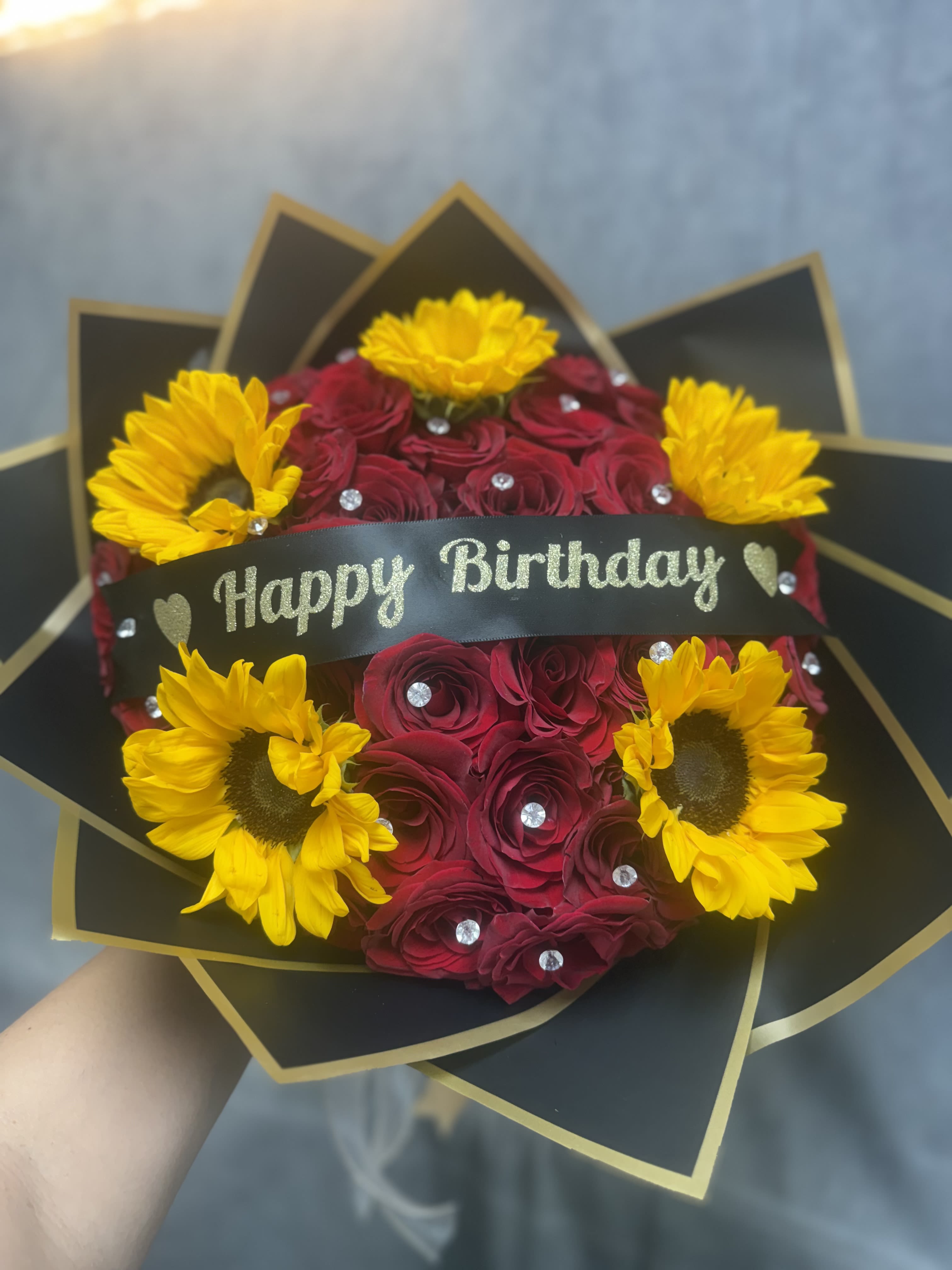 Sunny Rosy Birthday Bouquet - Celebrate their special day with our Sunny Rosy Birthday Bouquet! This cheerful design features luxurious red roses paired with bright sunflowers, accented with sparkling gems and a festive birthday ribbon. The perfect combination of elegance and happiness, this bouquet is sure to make any birthday extra memorable and bring a smile to their face. 