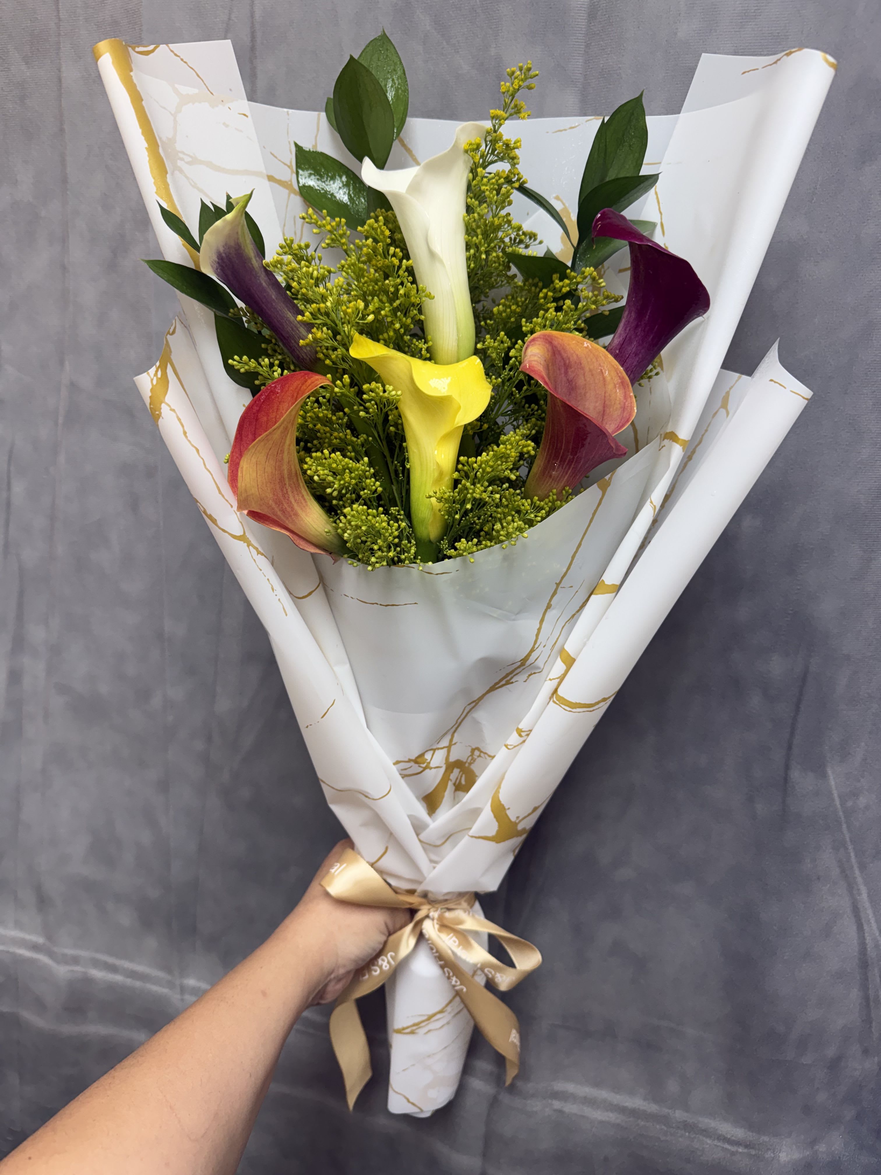 Calla Lilies Lovers Bouquet  - A stunning collection of six elegant calla lilies in a beautiful mix of colors, accented with fresh greenery and golden solidago. Wrapped in our signature luxury paper and finished with a satin ribbon, this bouquet is a graceful and sophisticated gift for birthdays, anniversaries, celebrations, or simply to brighten someone’s day. 