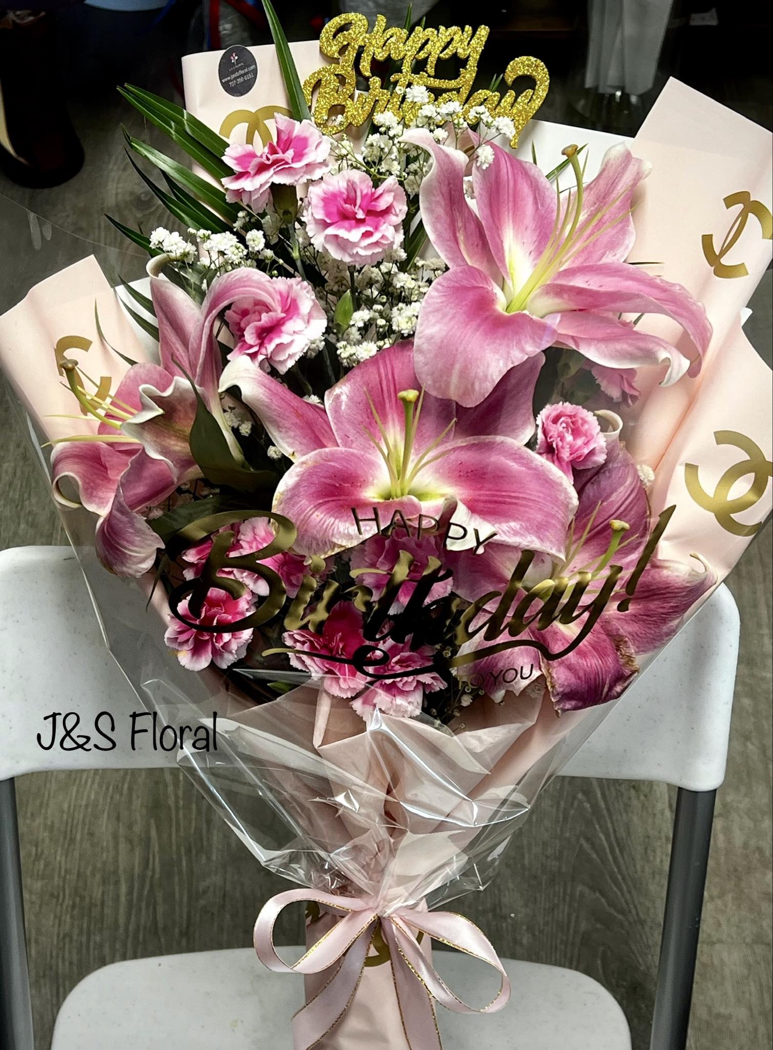 Pink lilies and carnations in a wrapped bouquet with a birthday topper