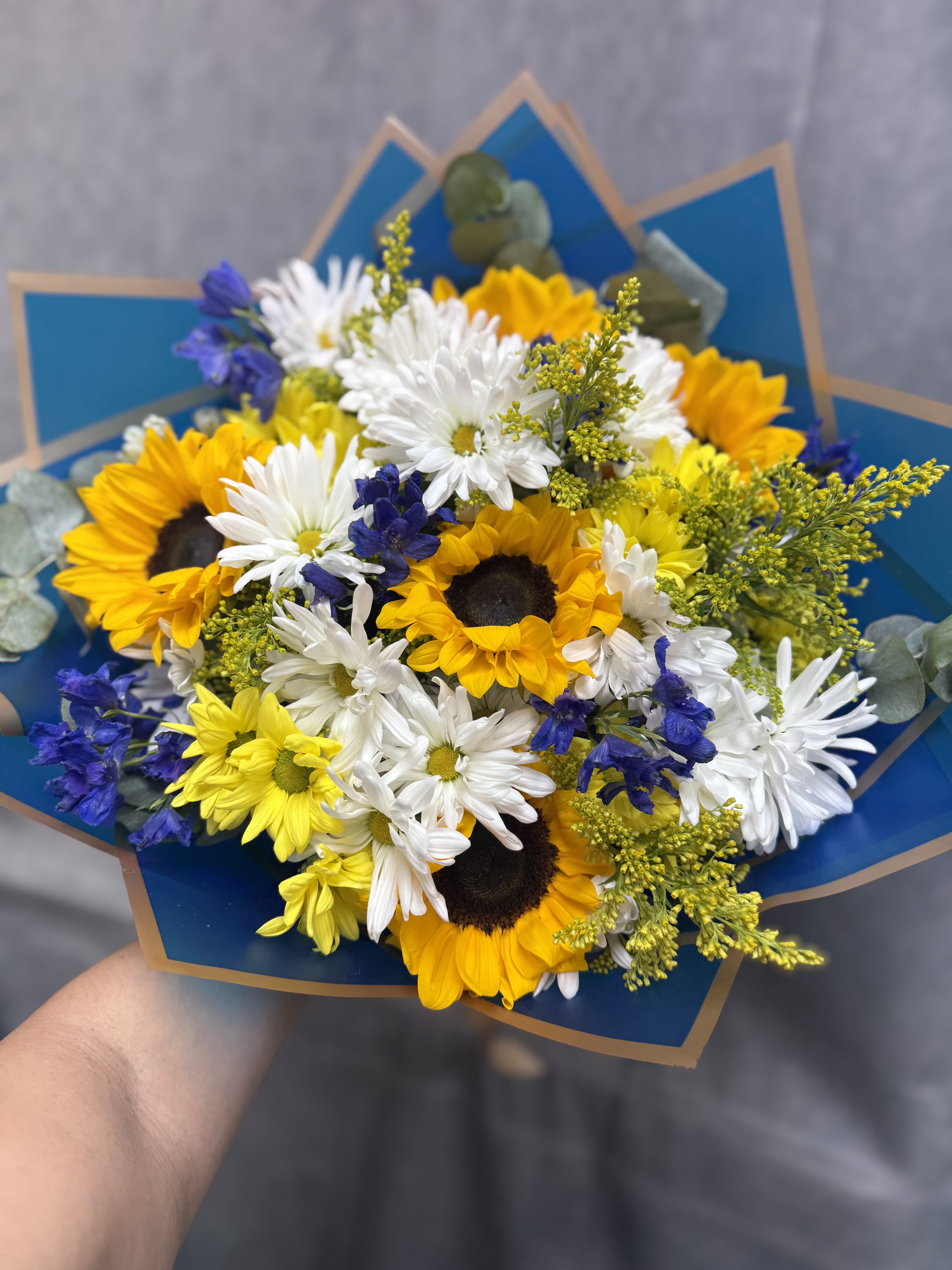 The Starry Night Bouquet  - Inspired by Van Gogh, this stunning arrangement features sunflowers, daisies, delphiniums, and waxflowers in a vibrant palette of blues, yellows, and whites. Perfect for adding artistic flair to any occasion, this bouquet celebrates creativity and beauty in every bloom.