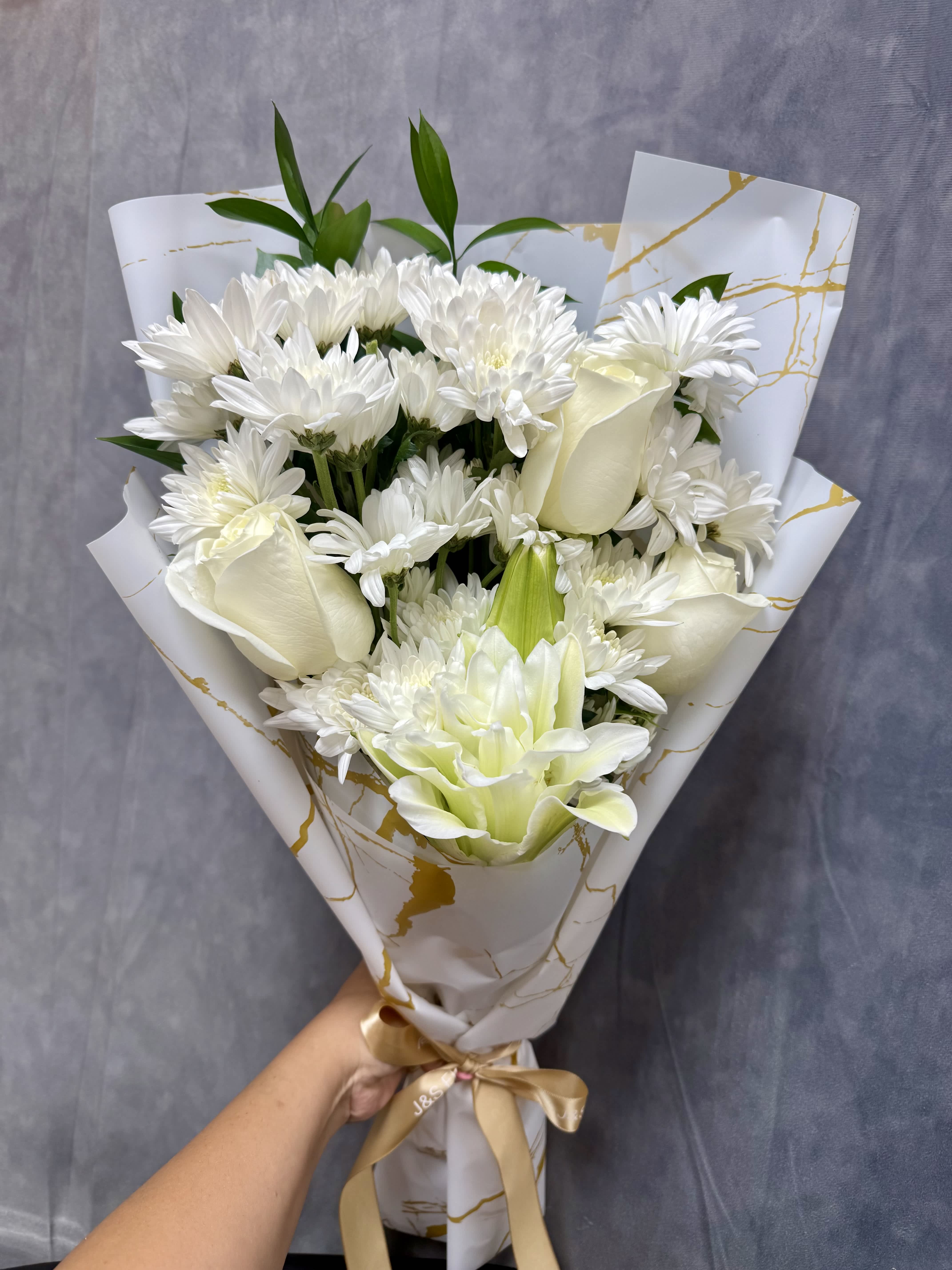 White bouquet with daisies, roses, and a lily wrapped in patterned paper