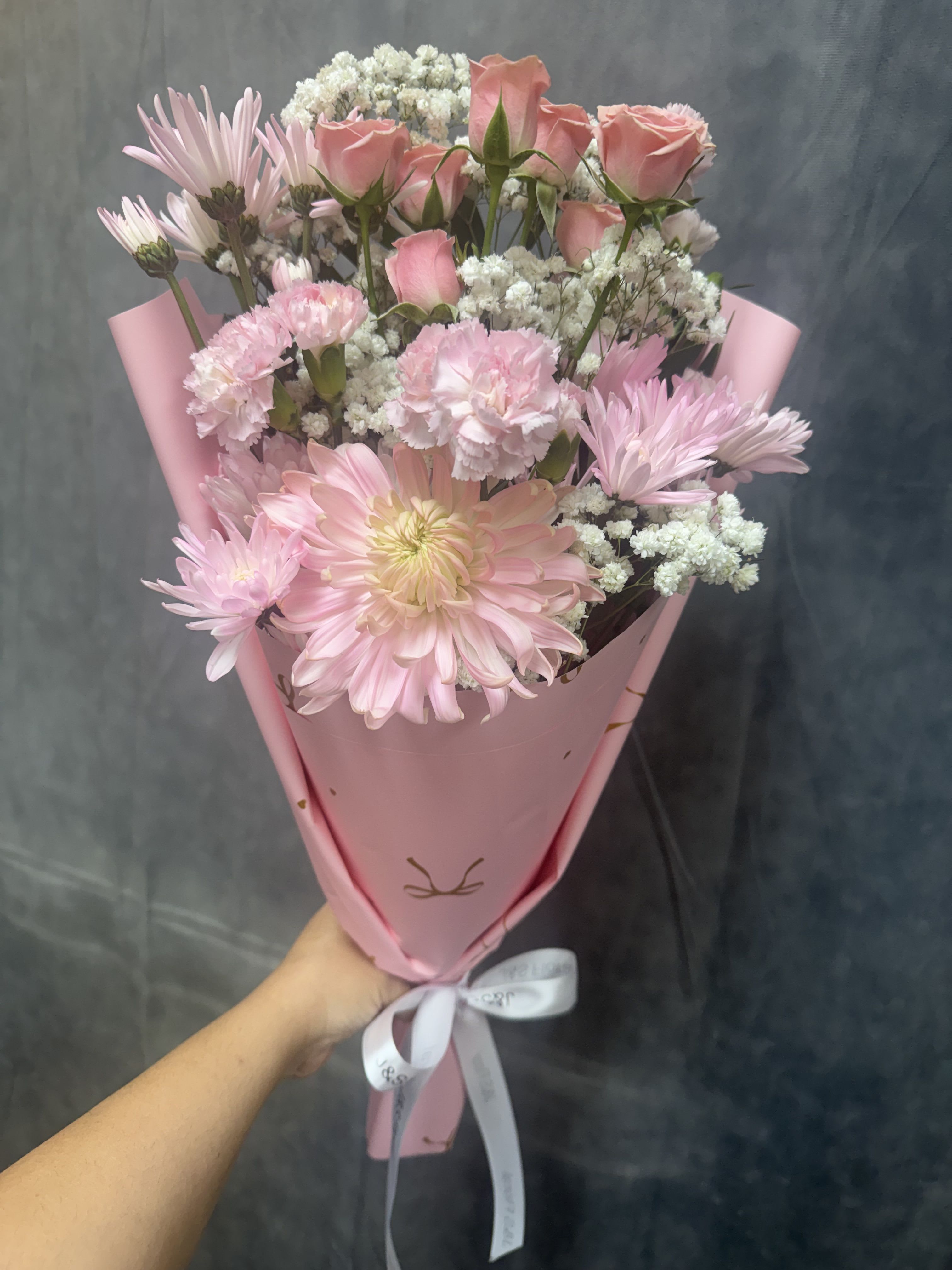 Welcome Baby Girl - Soft pink roses, daisies and carnations with white filler and green accents, wrapped in pastel pink paper and tied with a white ribbon-sweet, feminine bouquet for welcoming a baby girl.