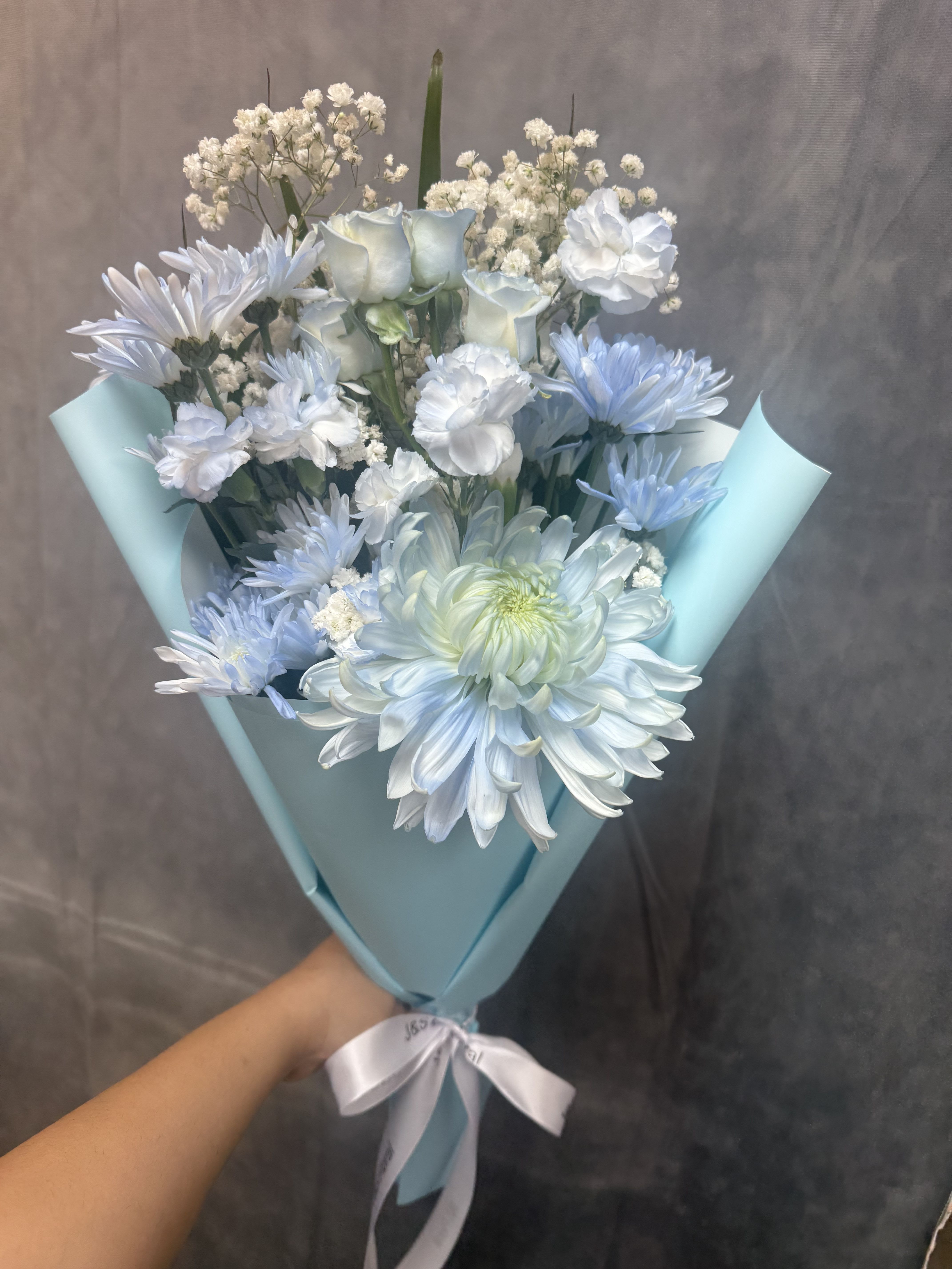 Welcome Baby Bouquet - Pale blue, white and green bouquet of chrysanthemums, roses and carnations, hand-tied with light blue wrap and white satin ribbon-soft, airy and perfect for welcoming a new baby.