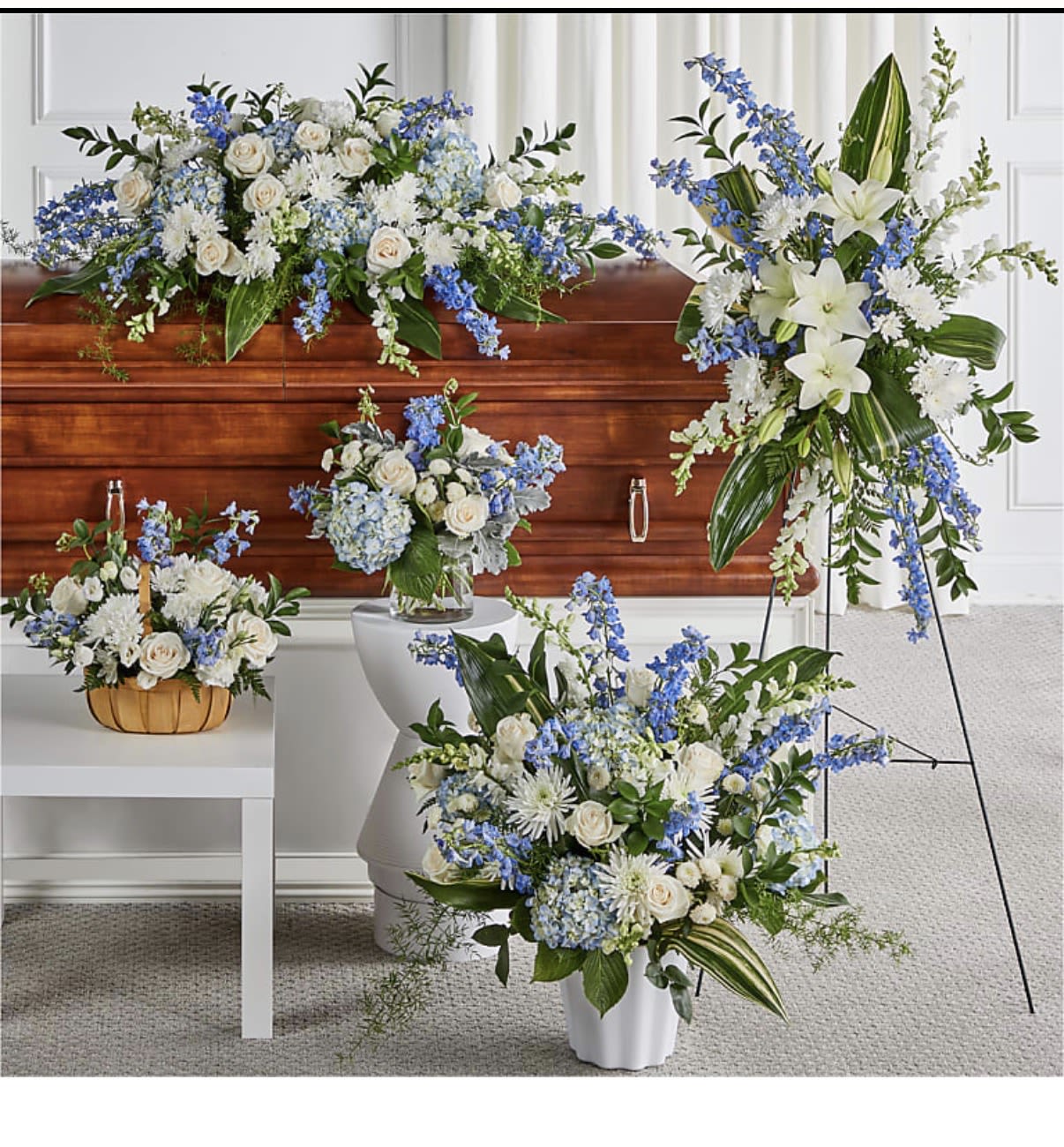 Collection of white and blue funeral flower arrangements around a wooden casket.