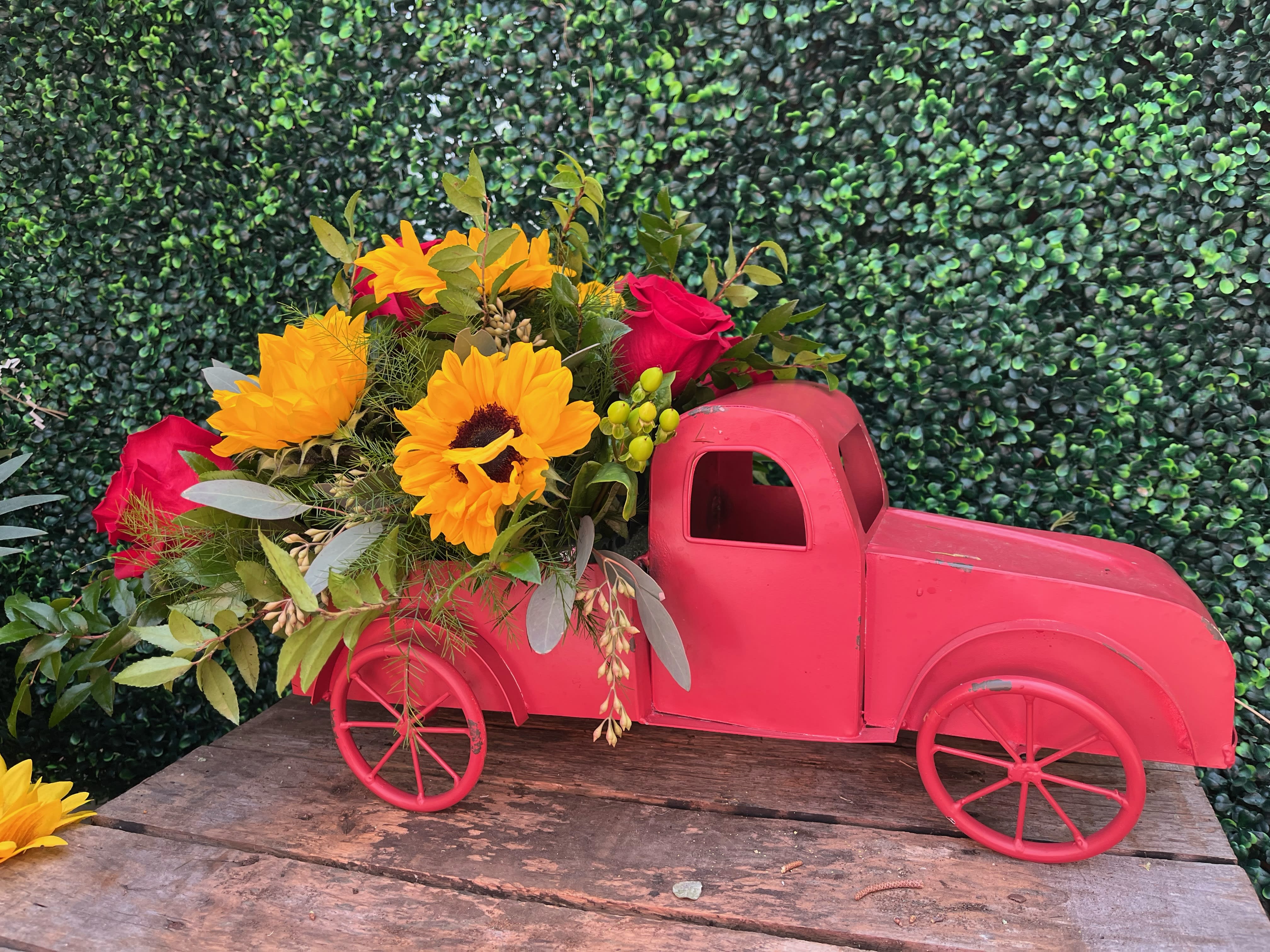 Pink toy truck filled with sunflowers and red roses