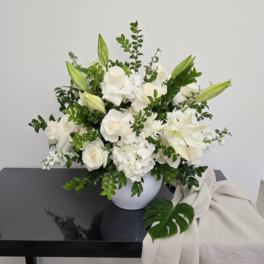 White floral arrangement in a round vase with lilies and roses