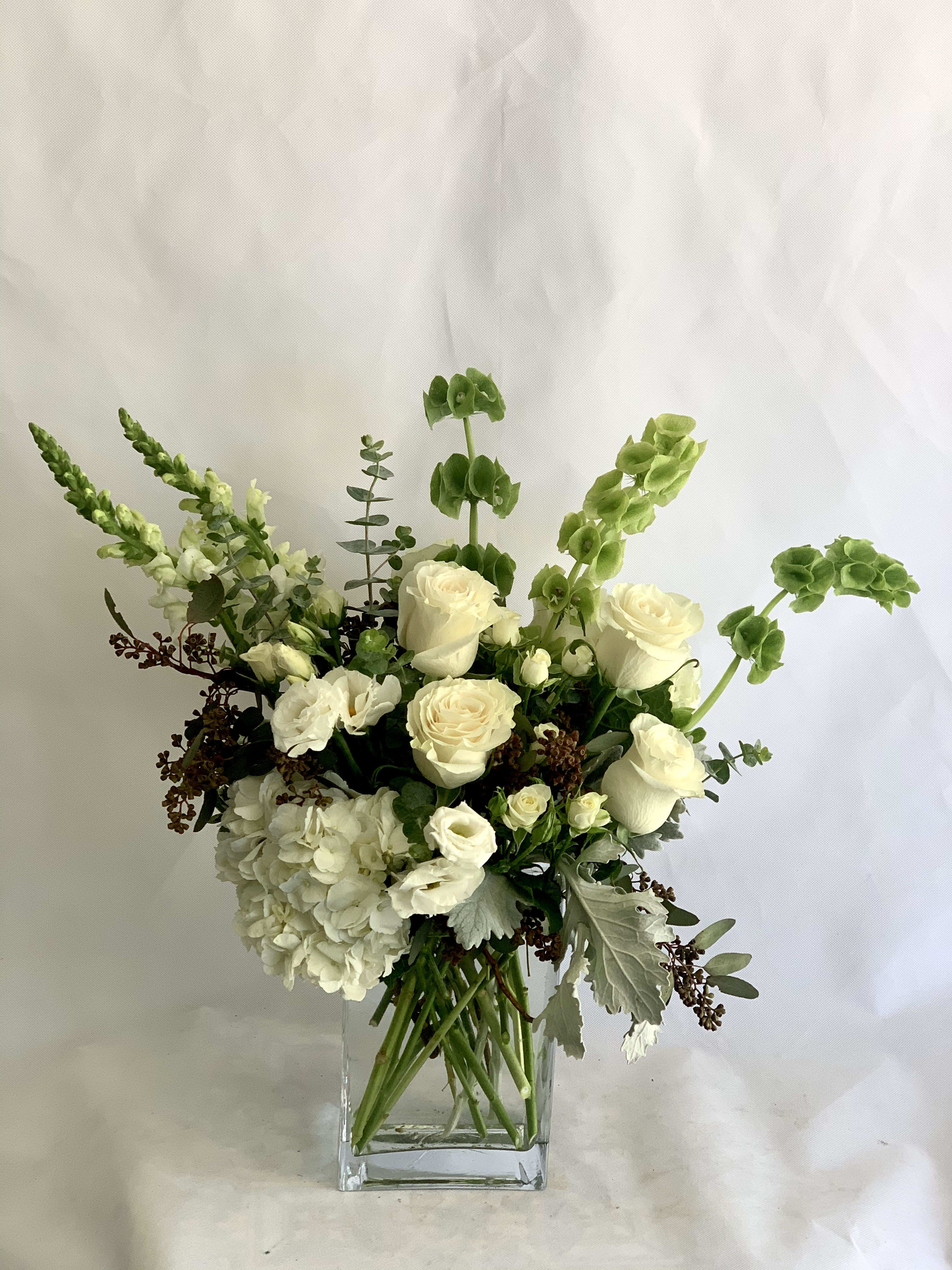 White floral arrangement in a clear square vase with tall green accents