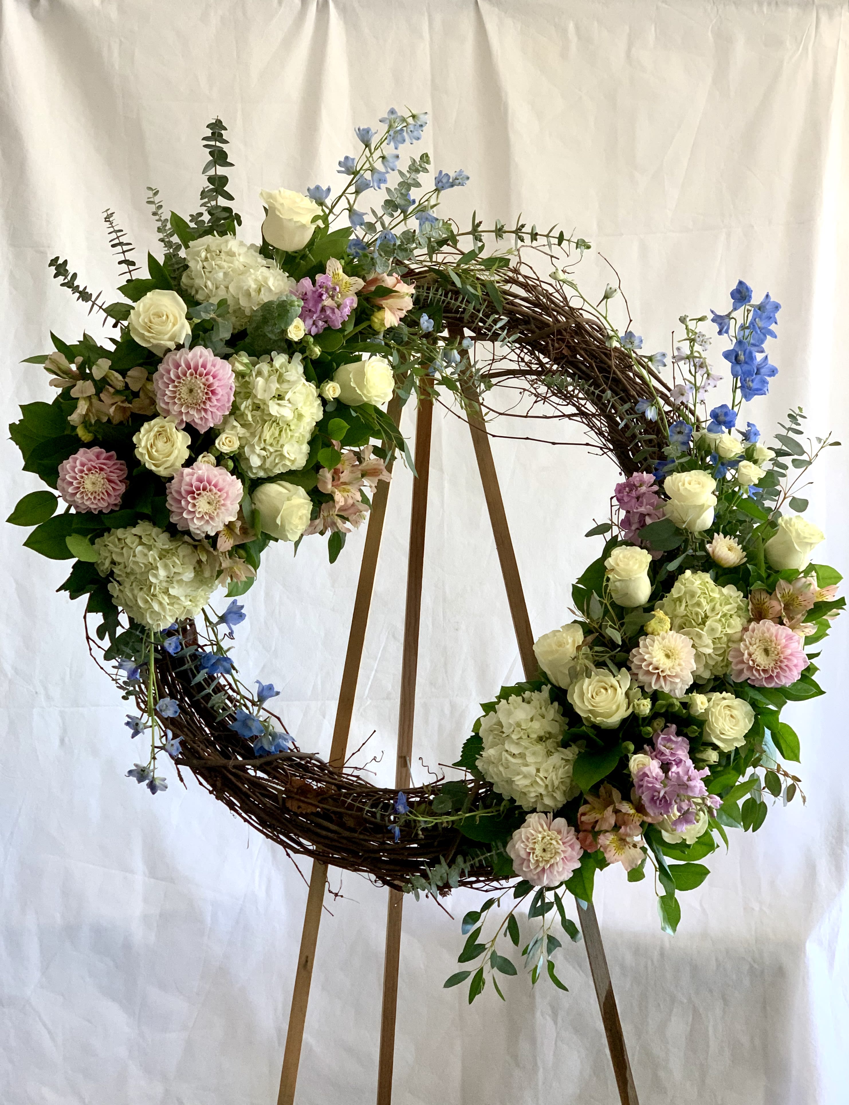 Large floral wreath with white, pink, and blue flowers on a wooden stand