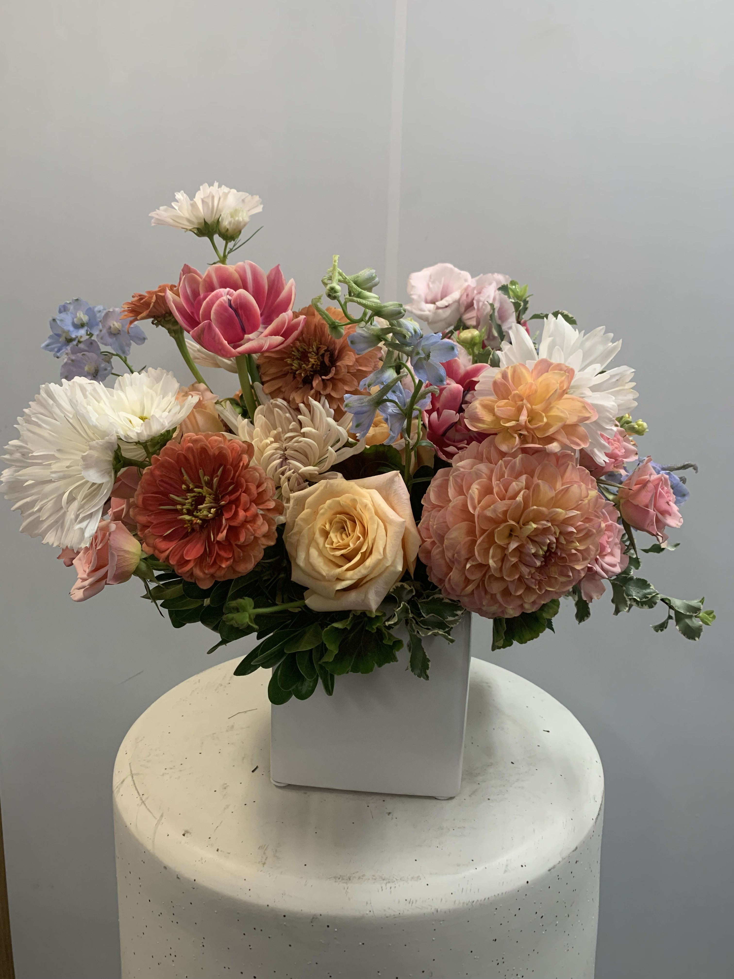 Mixed bouquet of pastel flowers in a white square vase