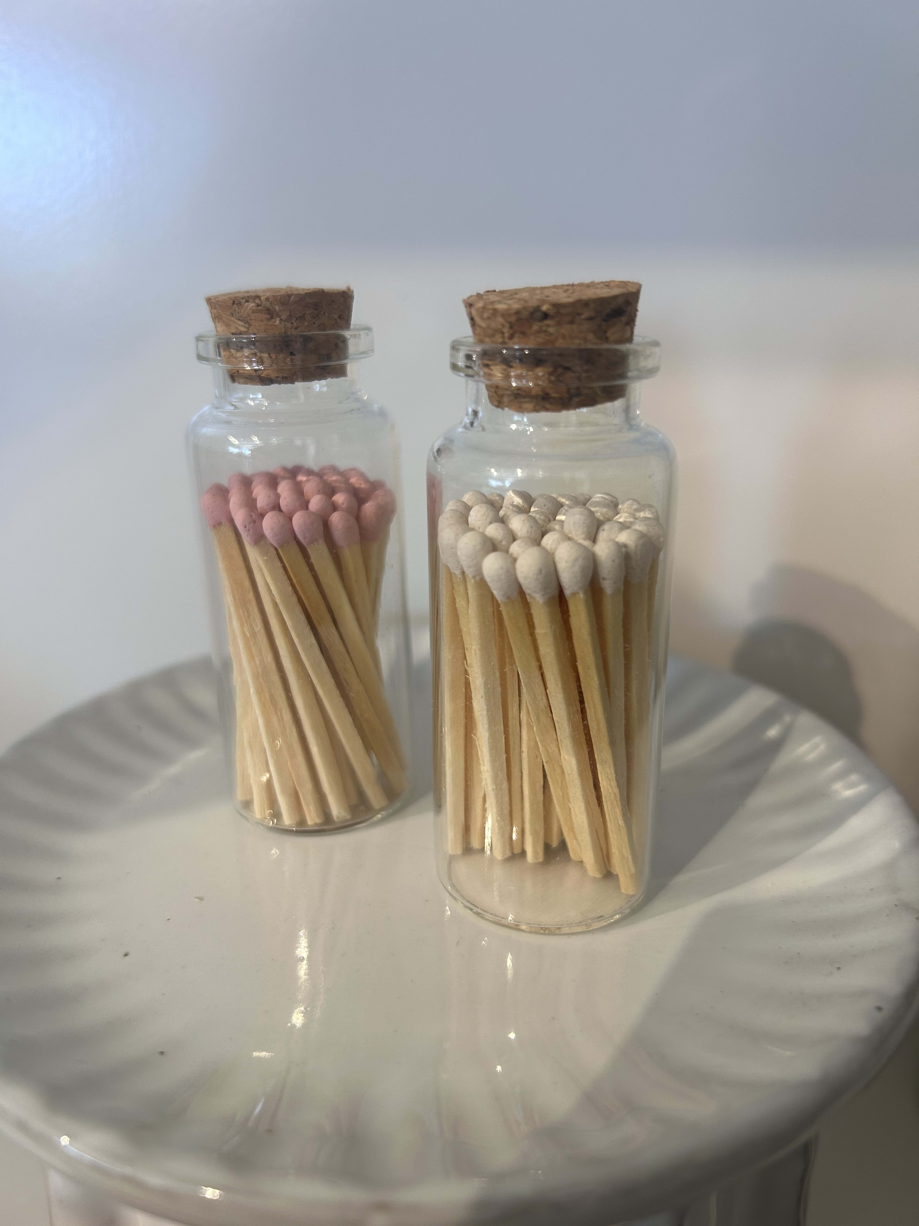 Two glass bottles filled with wooden matches, one with pink tips and one with white tips