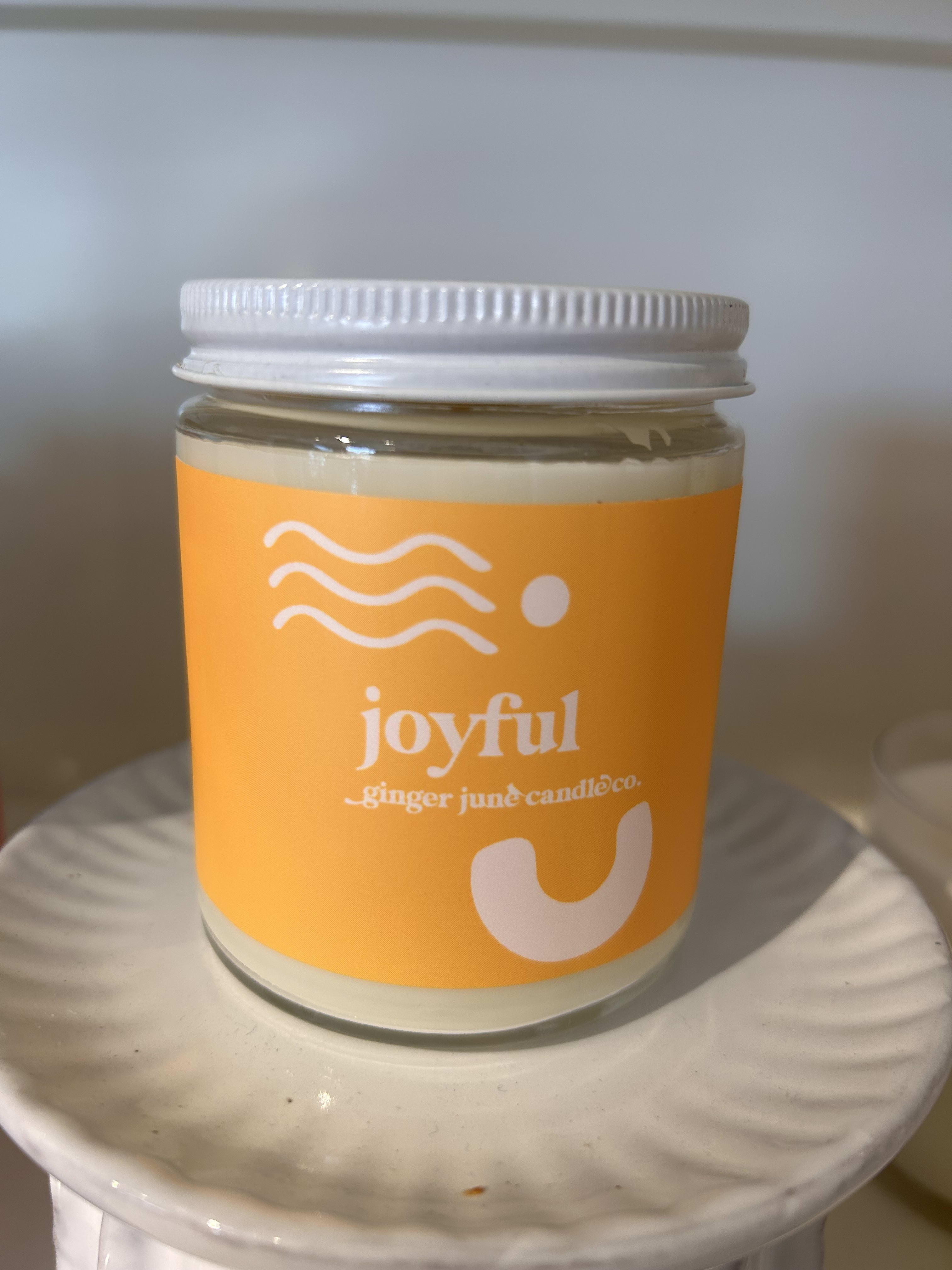 Glass jar candle with an orange label on a white surface
