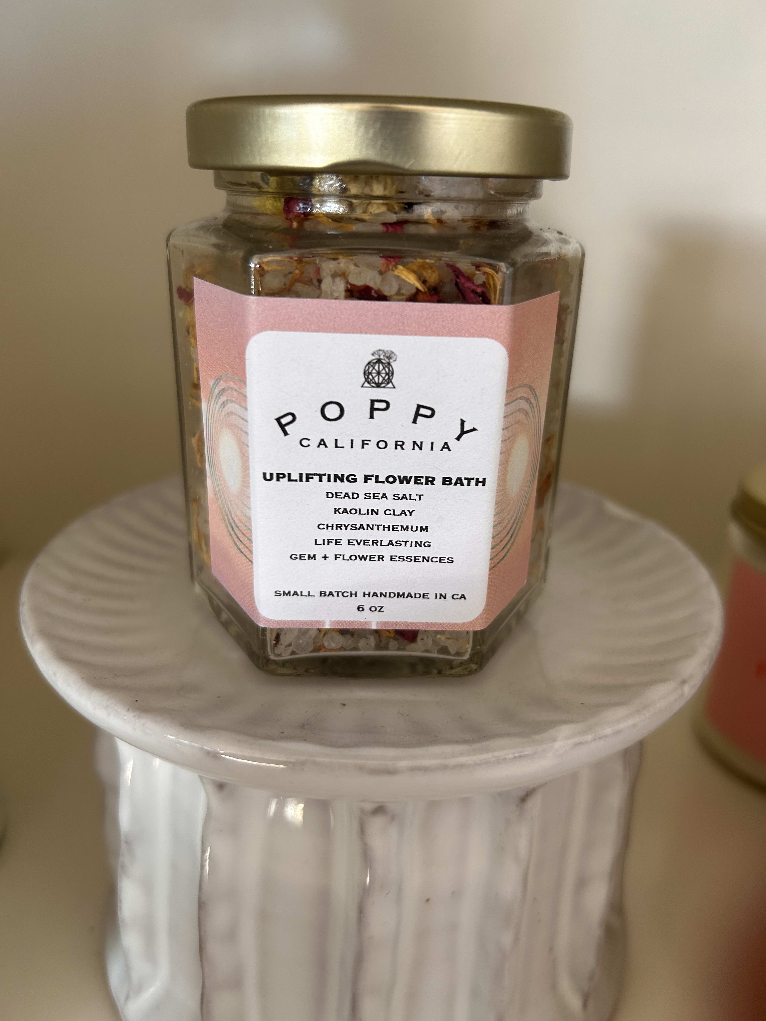 A glass jar of flower bath salts with a gold lid on a white pedestal