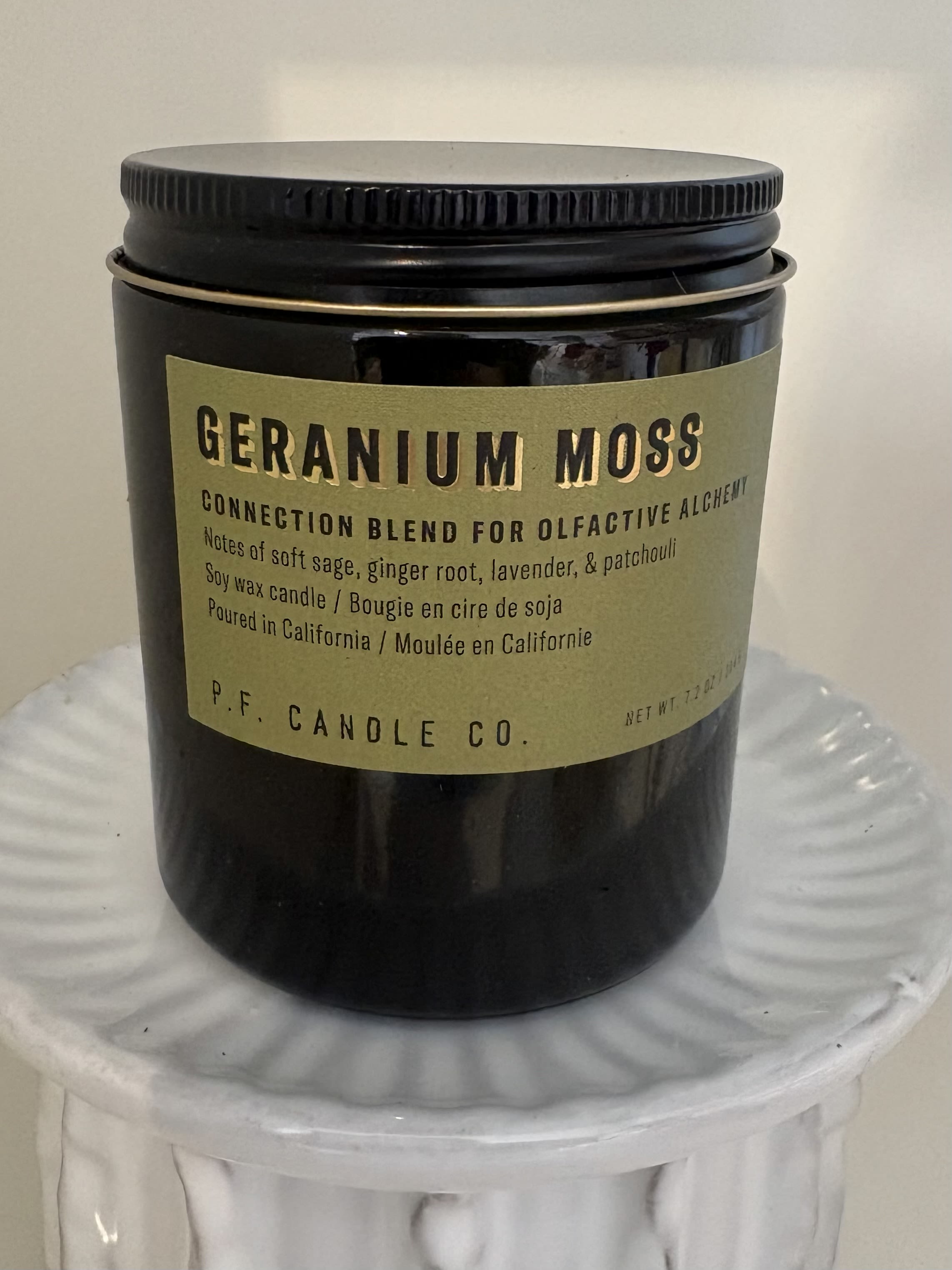 Black jar candle with a tan label on a white pedestal