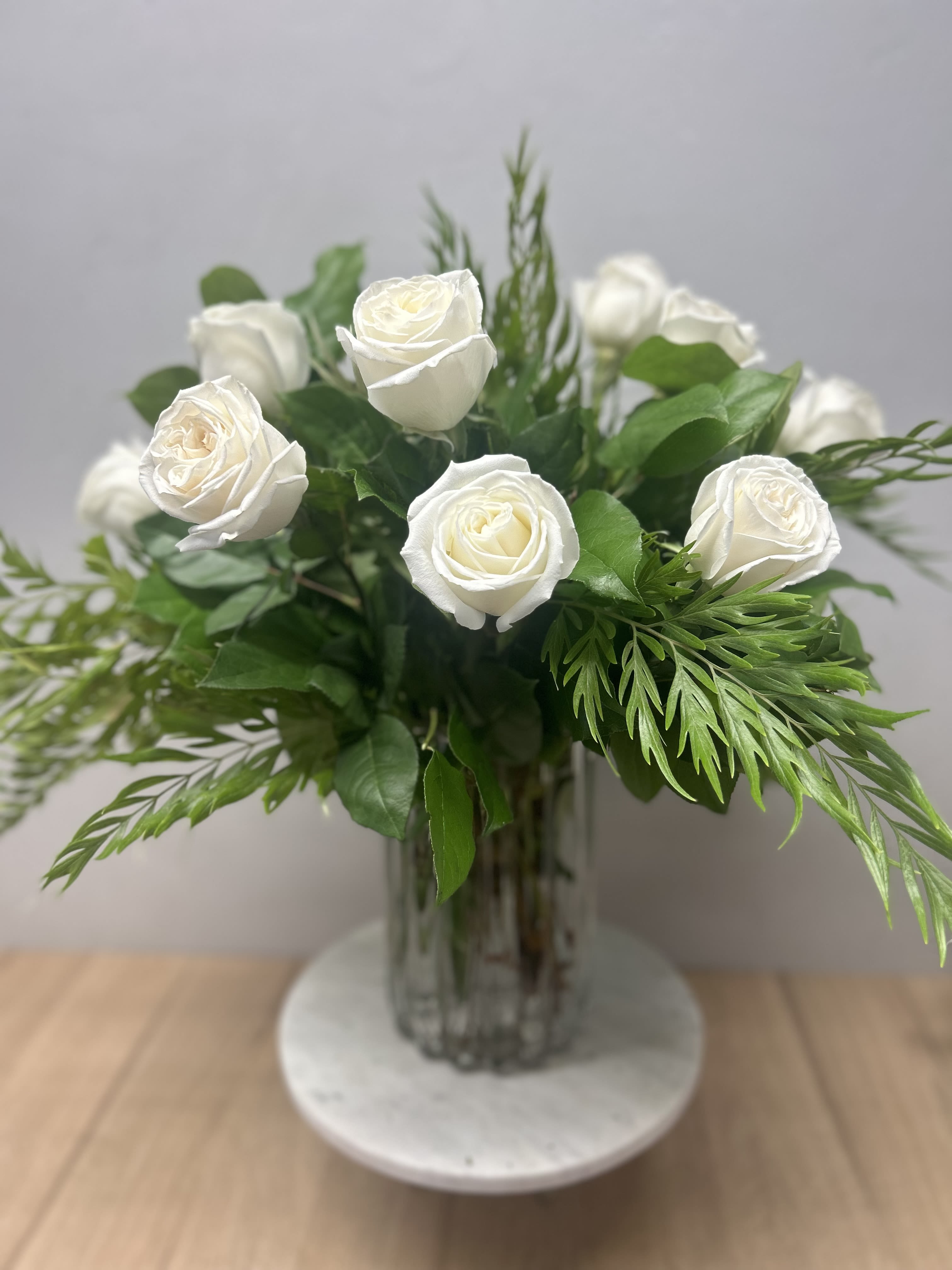 White roses arranged in a clear glass vase with green foliage