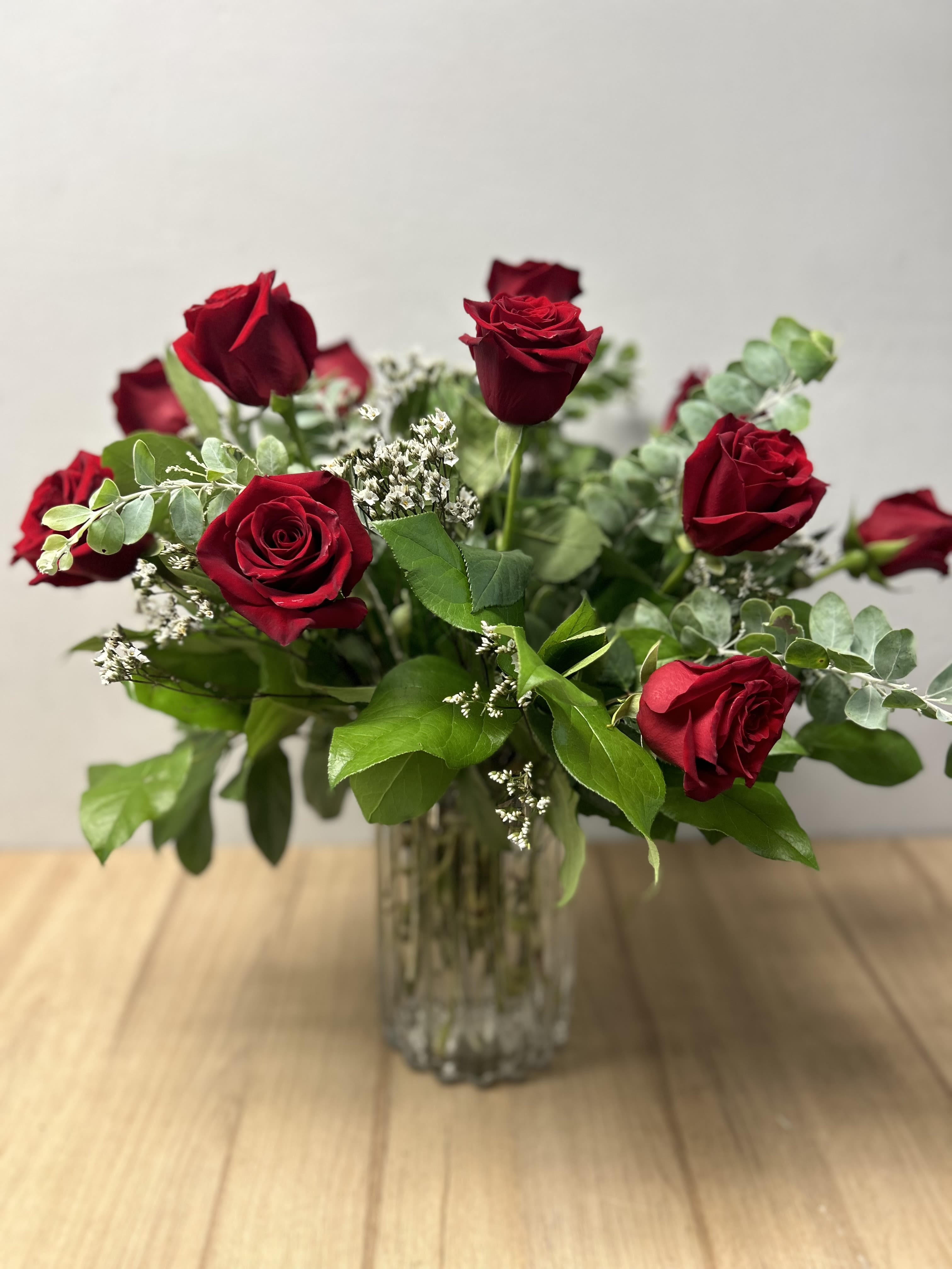 Red roses arranged in a clear glass vase with greenery