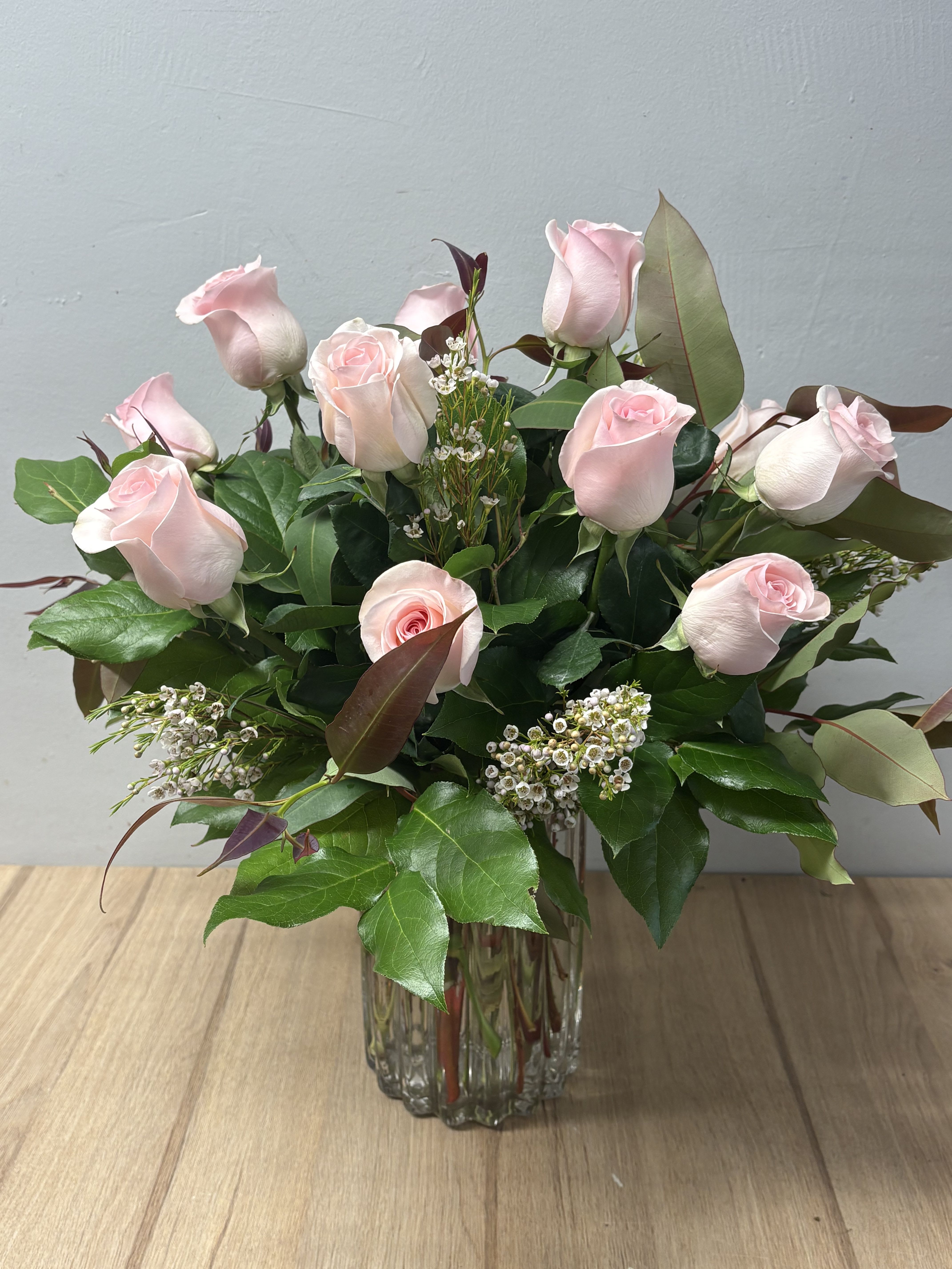 Pink roses arranged in a clear glass vase with greenery