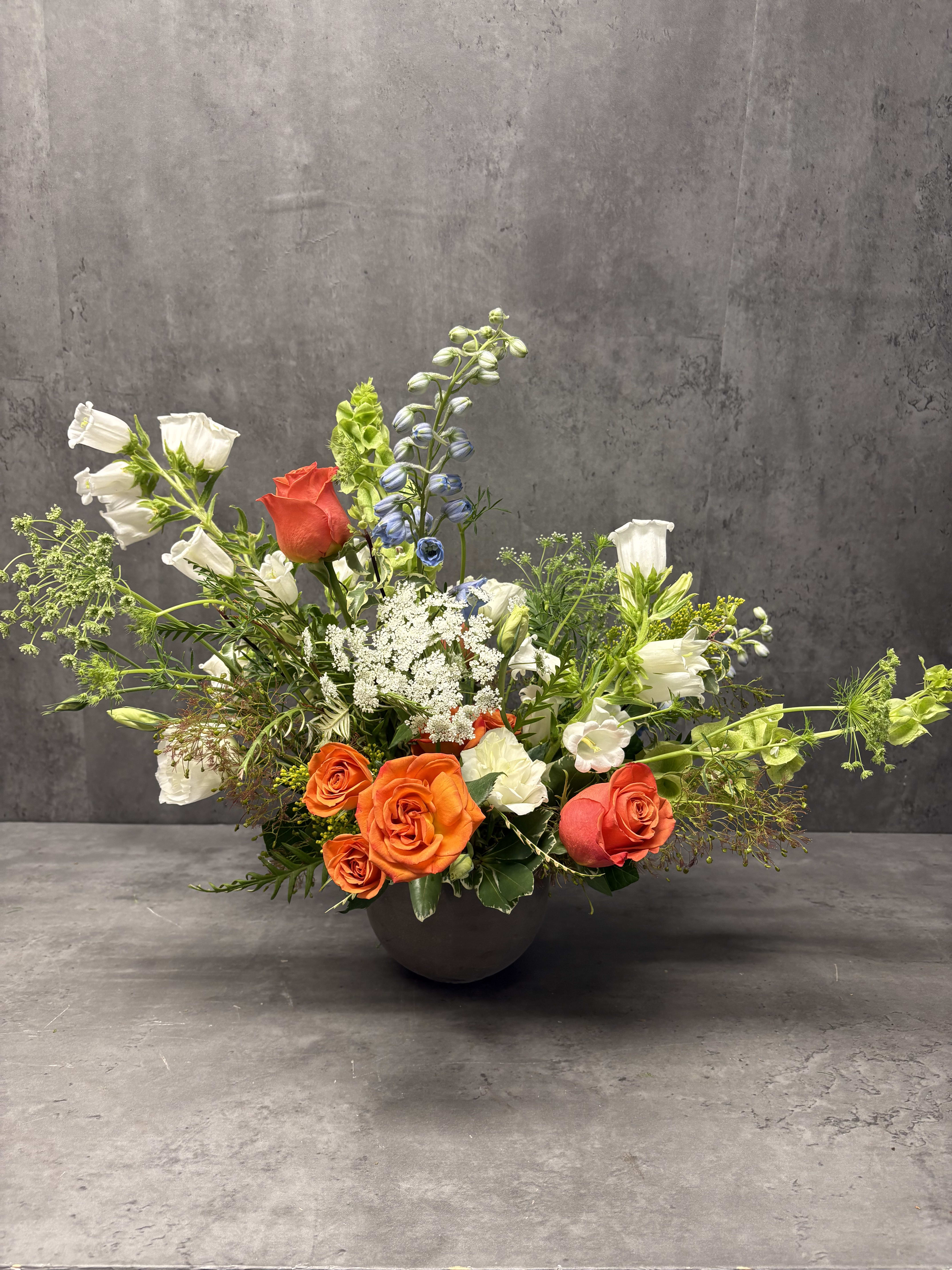 Mixed floral arrangement in a dark bowl vase with orange and white roses