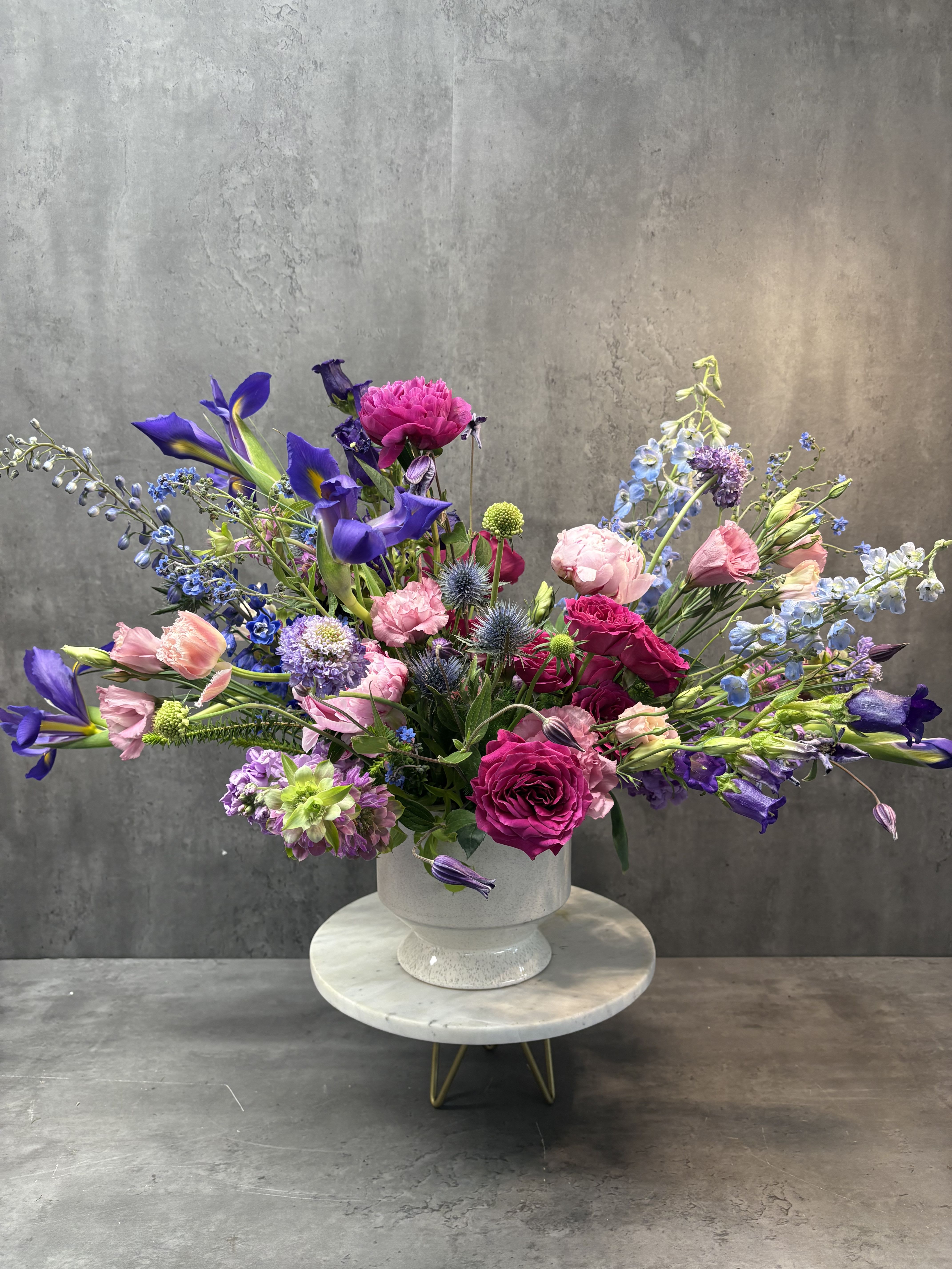 Large mixed bouquet of pink, purple, and blue flowers in a white pedestal vase