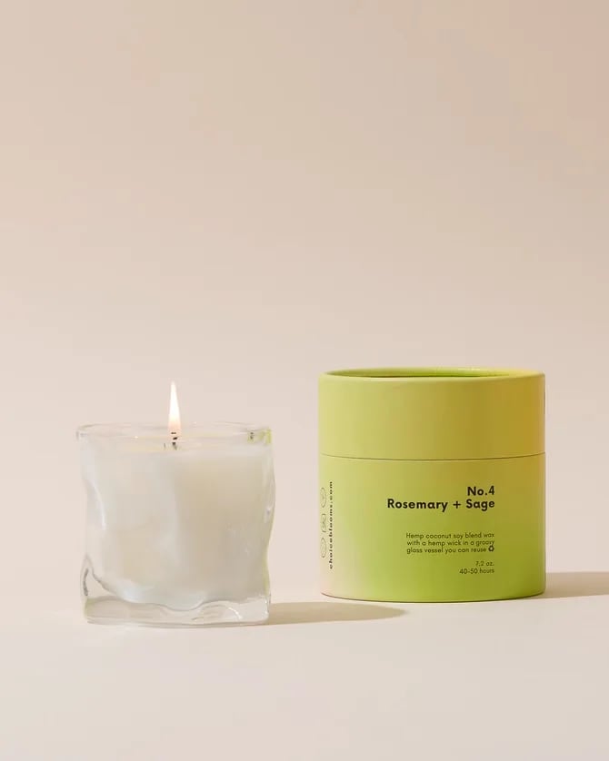 Lit white candle in a clear glass vessel beside a lime-green candle tin