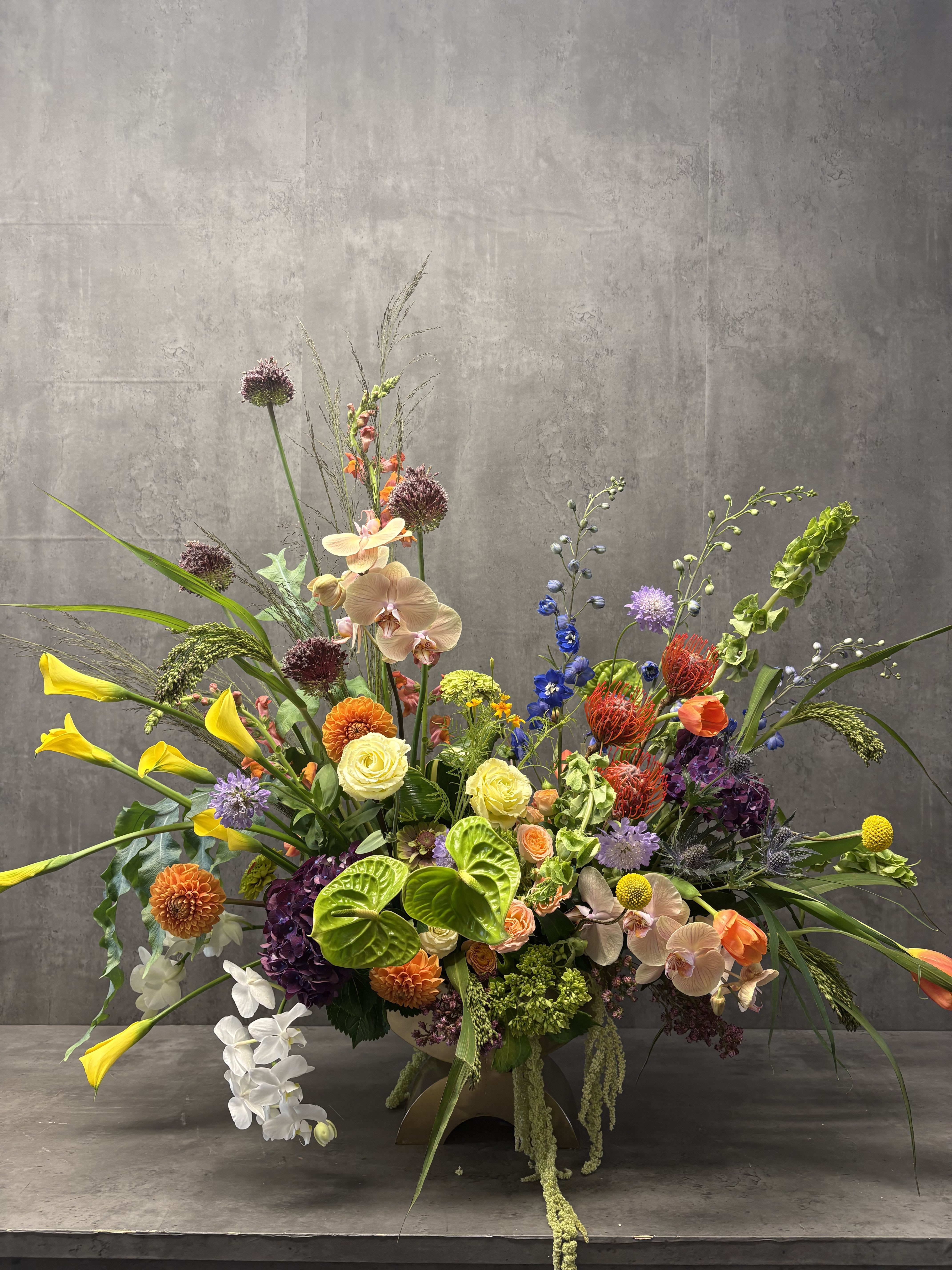 Large mixed floral arrangement with orchids, calla lilies, and bright accent blooms