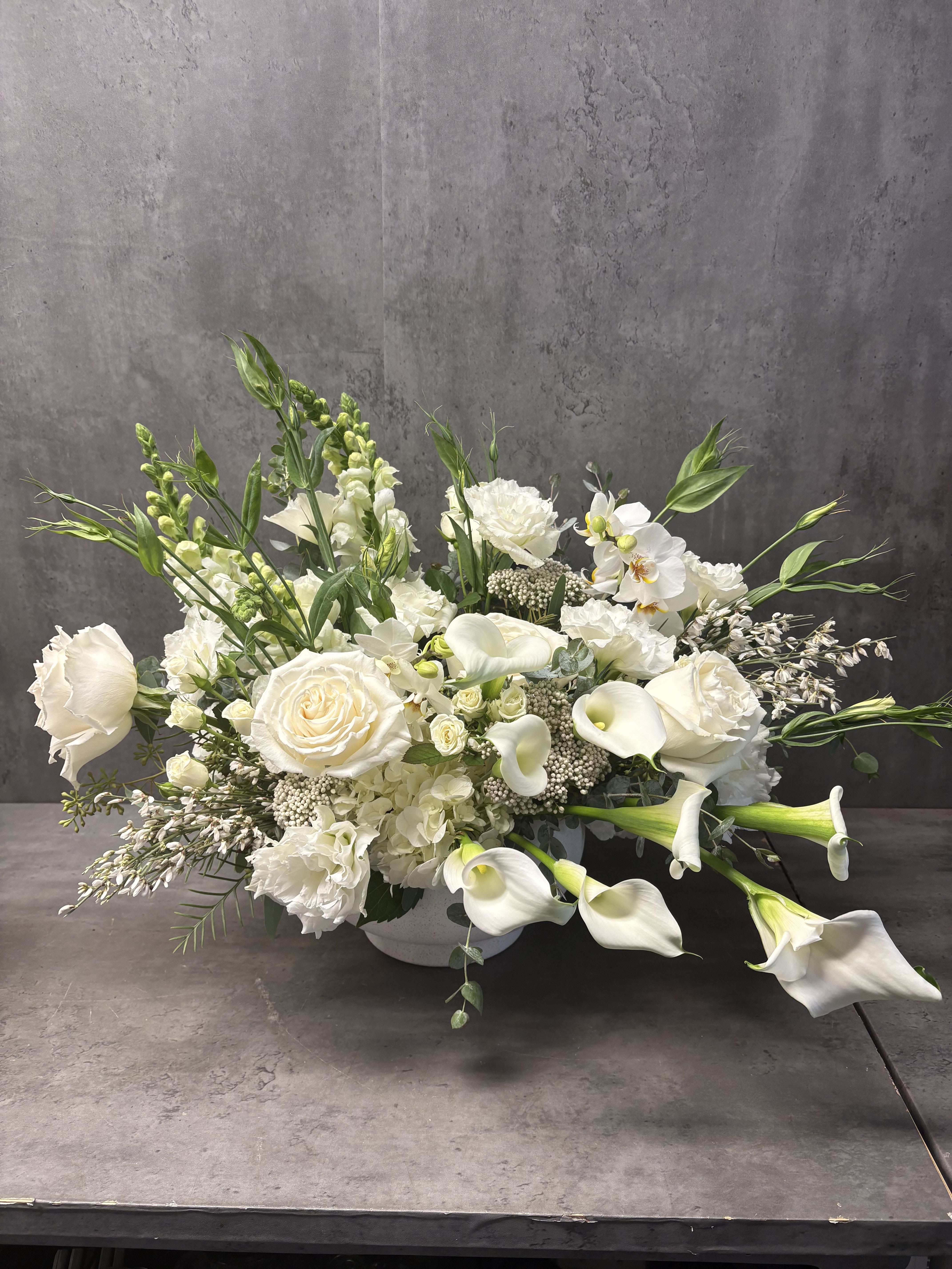 White floral arrangement with roses, calla lilies, and orchids in a low vase