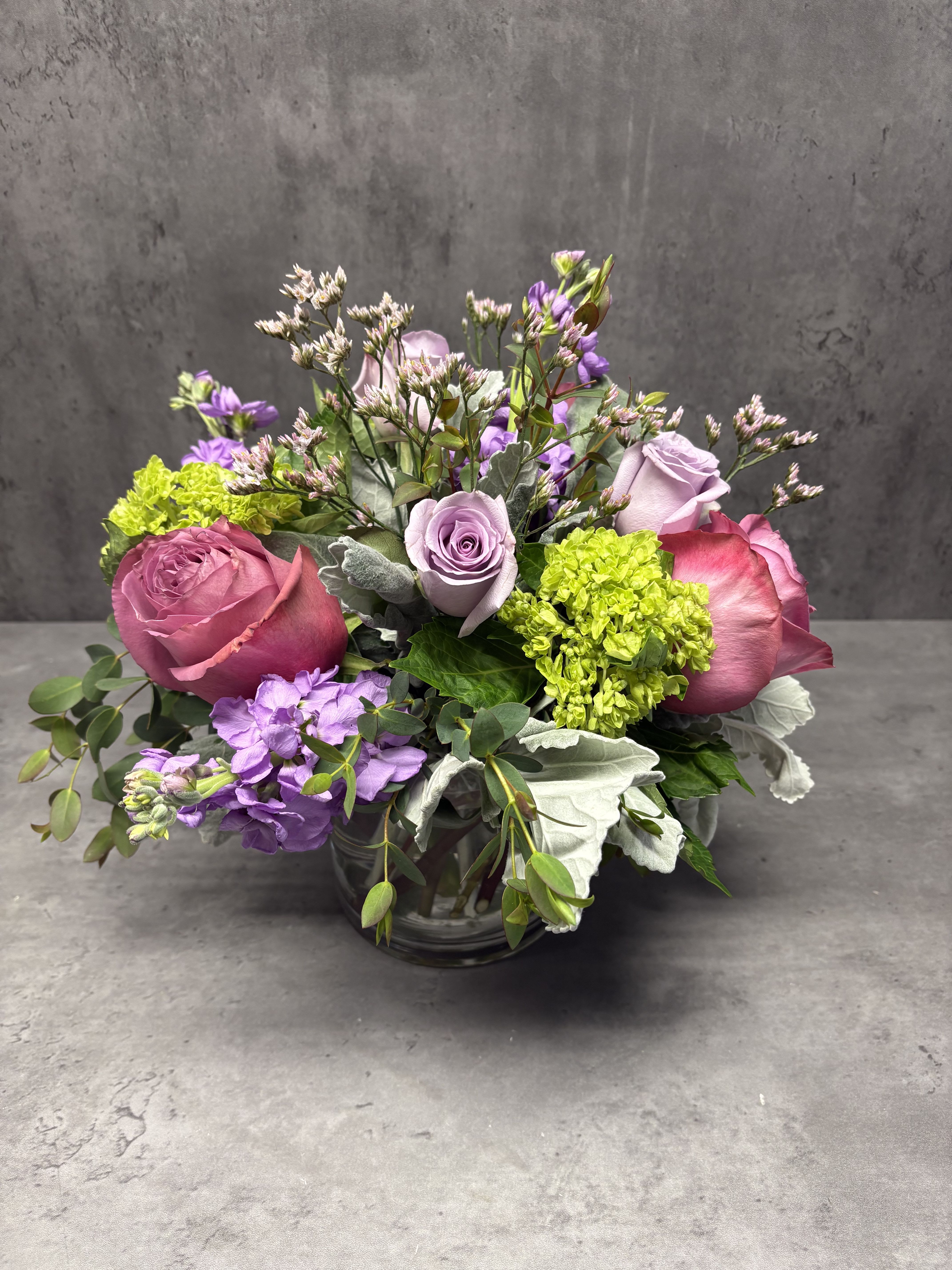 Pink and lavender roses arranged in a glass vase with purple blooms