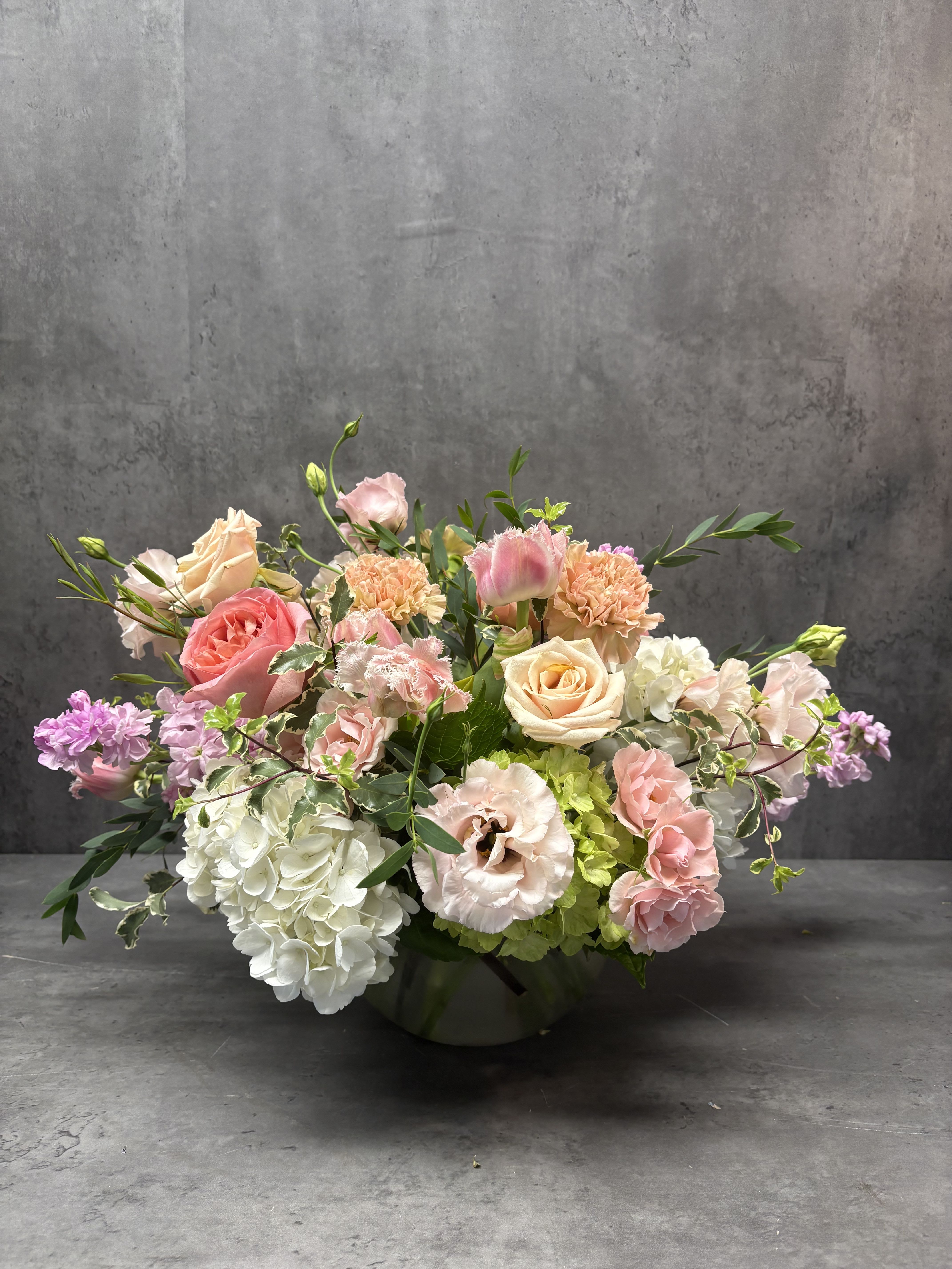 Pastel floral arrangement in a low vase with roses, hydrangeas, and carnations