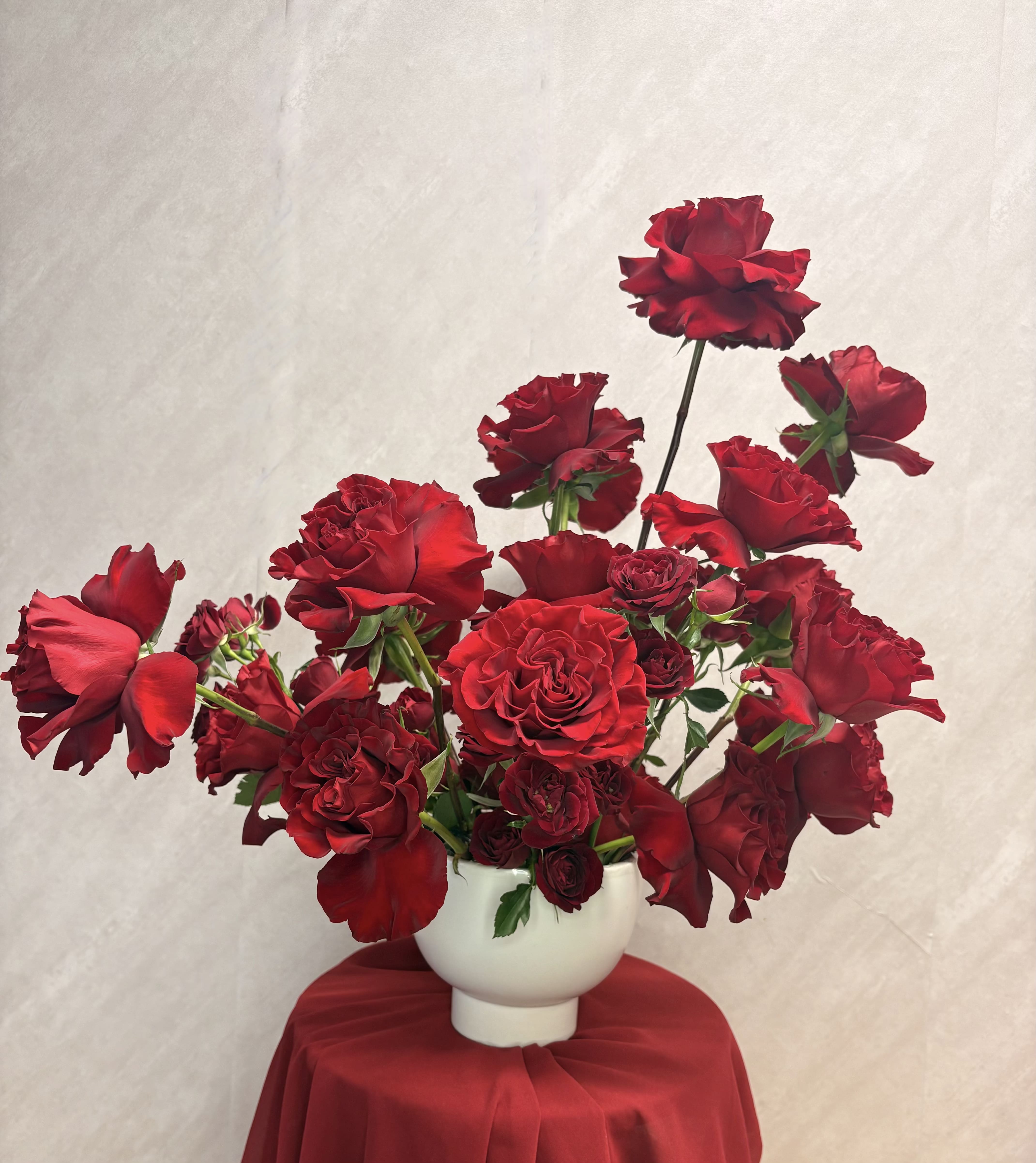 Red roses arranged in a white vase on a draped table