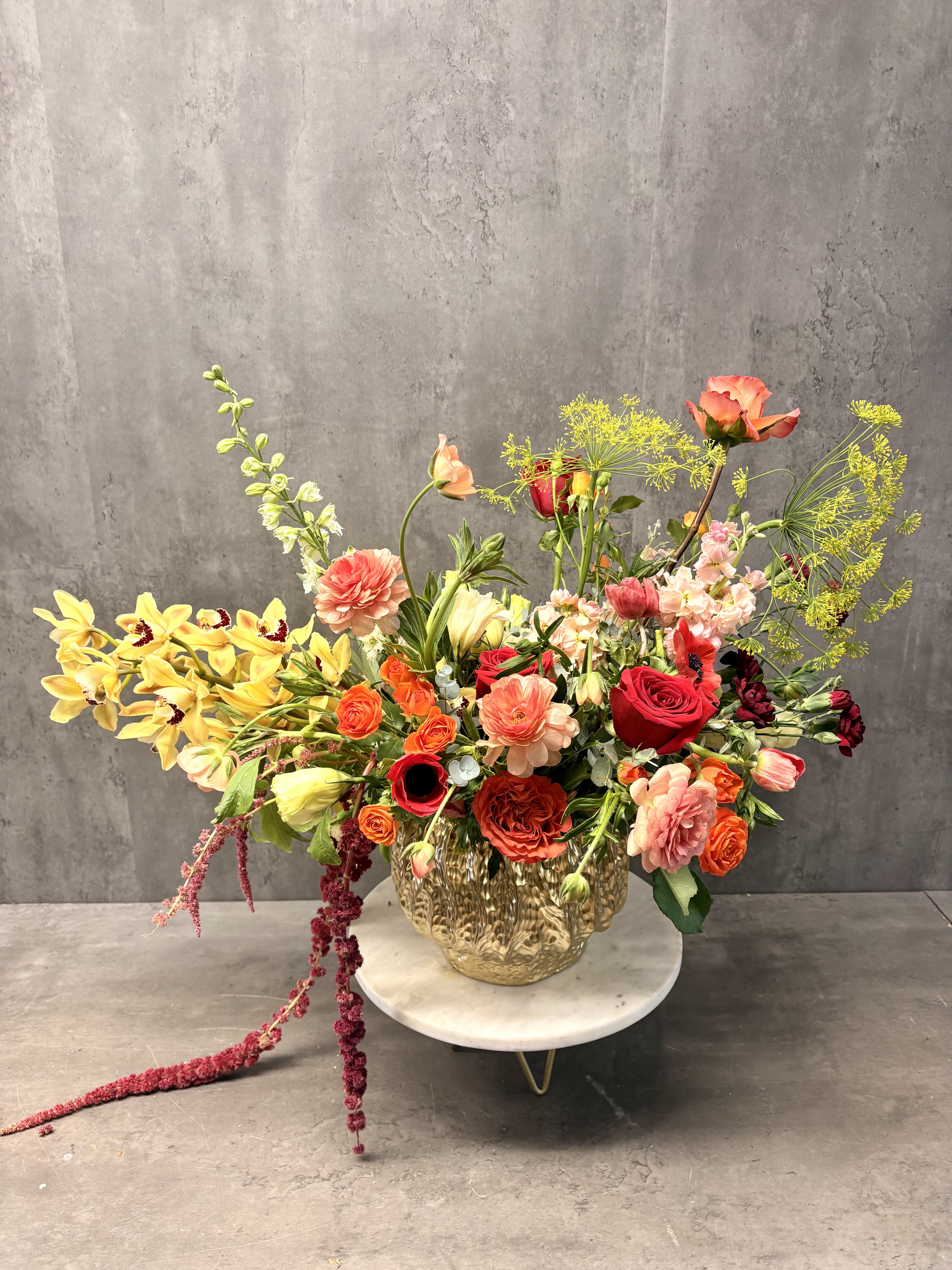 Large mixed flower arrangement in a gold vase on a white stand