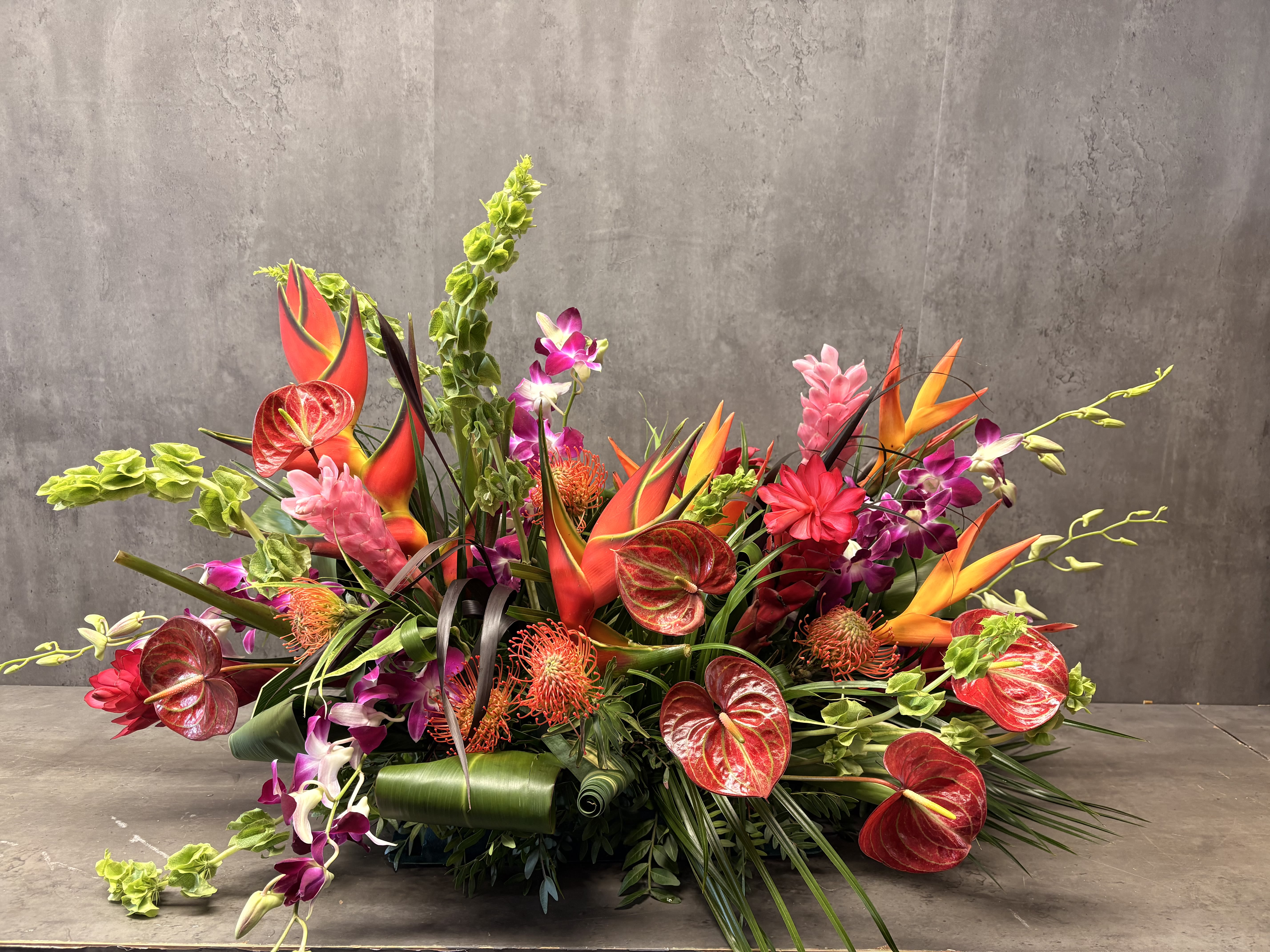 Tropical floral arrangement with orange heliconia, red anthuriums, and purple orchids