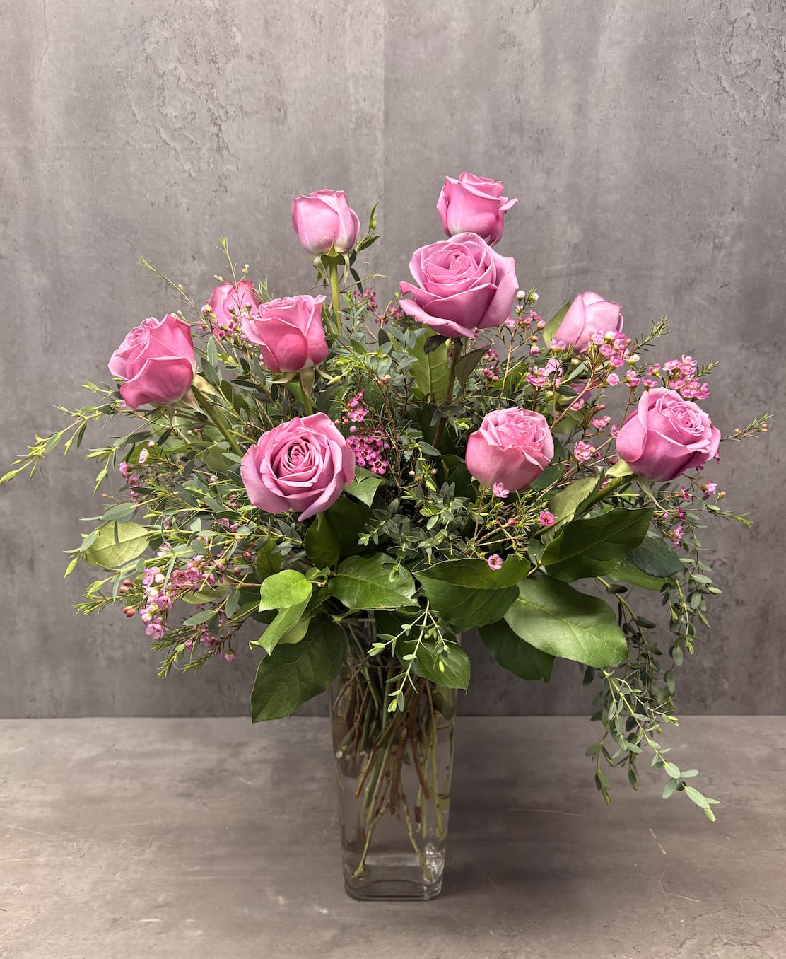 Pink roses arranged in a clear glass vase with small pink filler flowers.