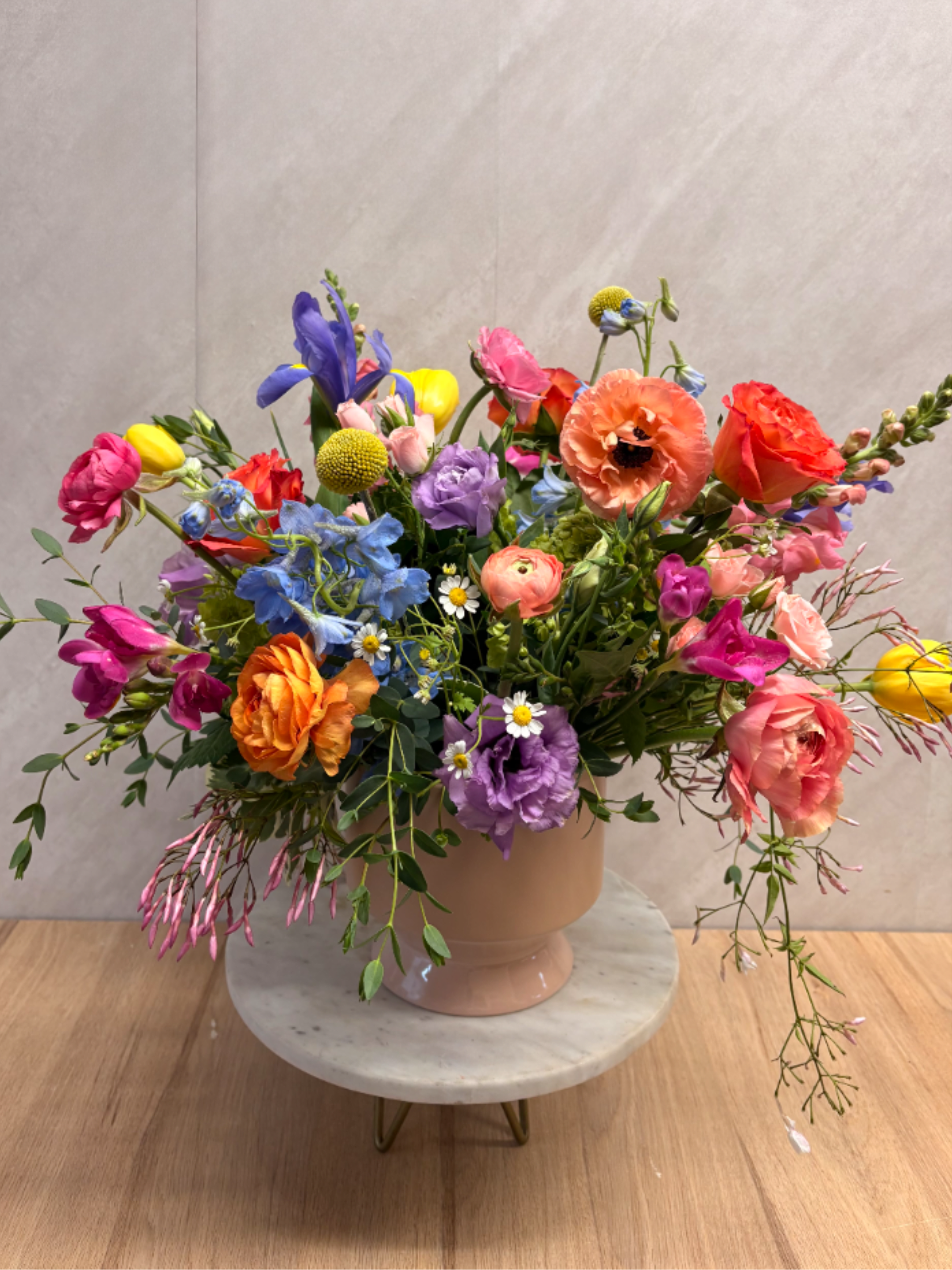 Colorful mixed flower arrangement in a blush ceramic vase on a marble stand
