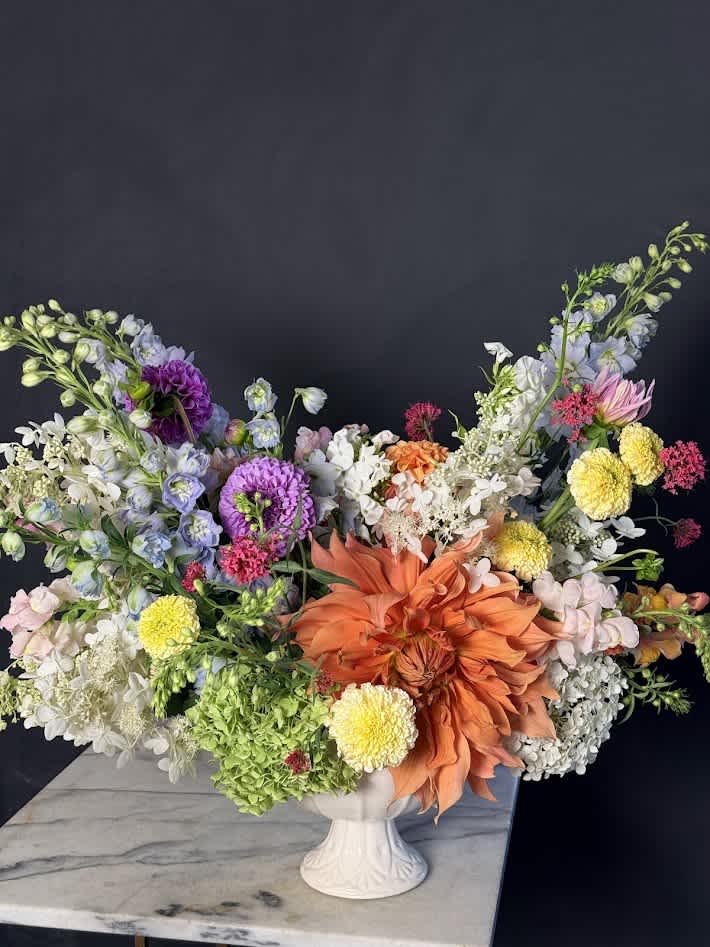 Large mixed flower arrangement in a white pedestal vase