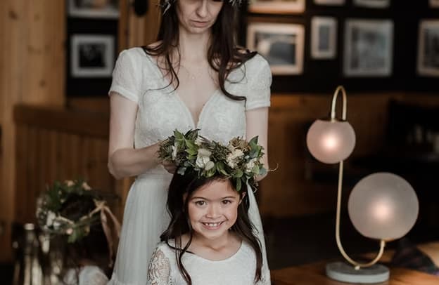 Bride adjusting a floral crown on a smiling girl in a white dress