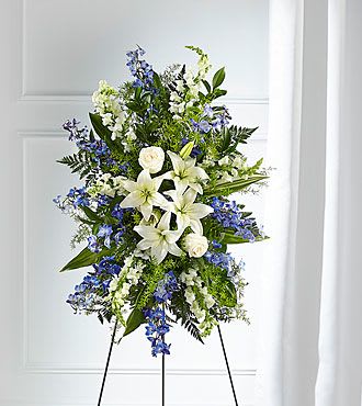 Tall standing spray of white lilies and blue flowers arranged on a metal easel
