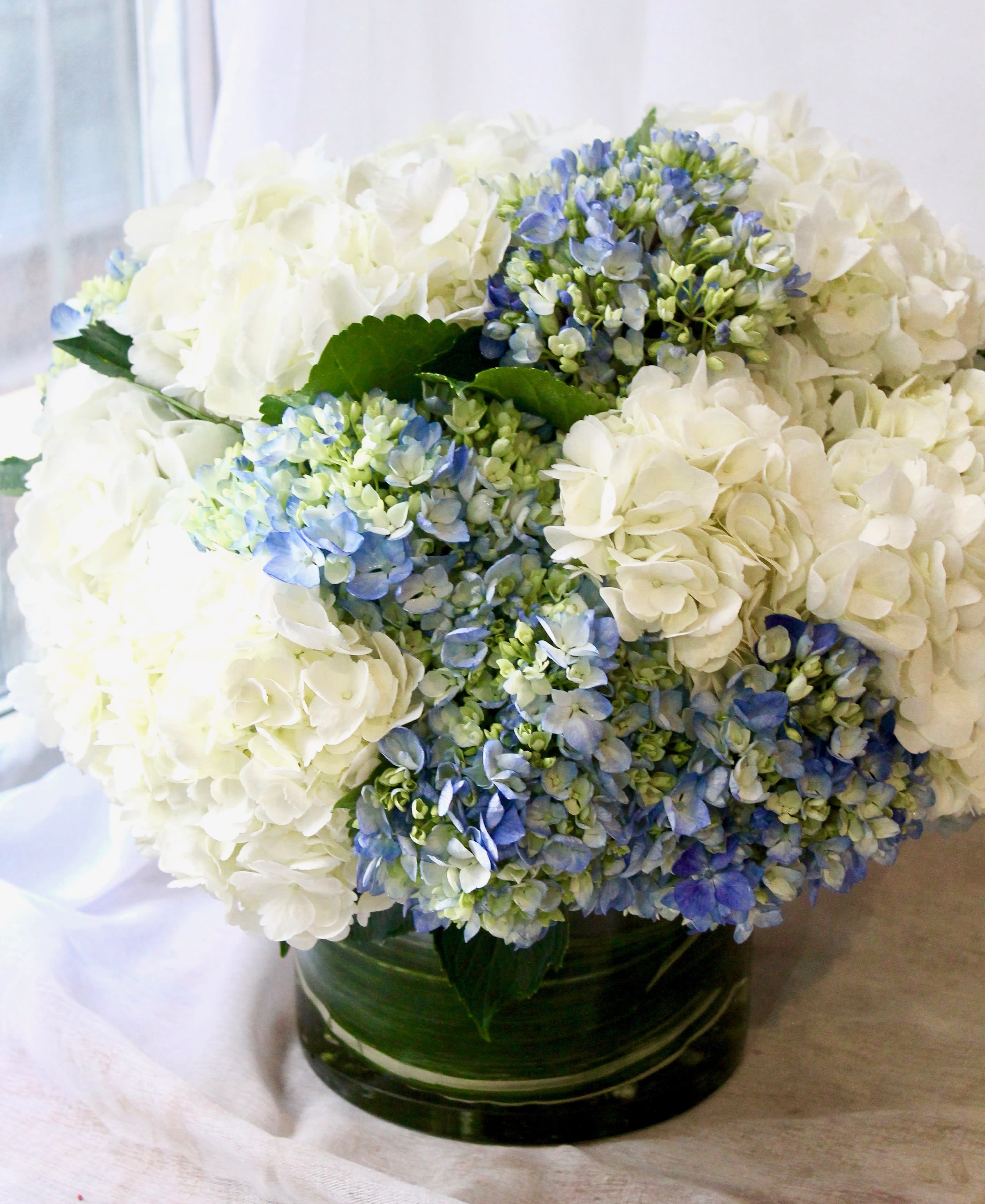 White and blue hydrangea arrangement in a green glass vase