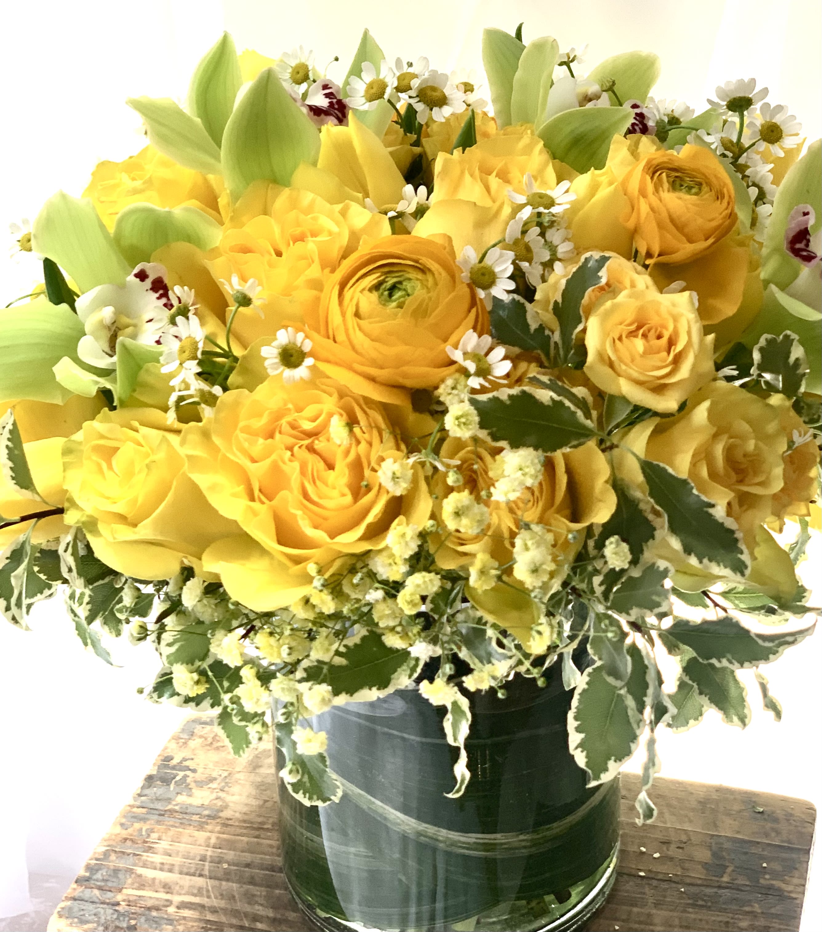 Yellow roses and ranunculus in a glass vase with small white daisies