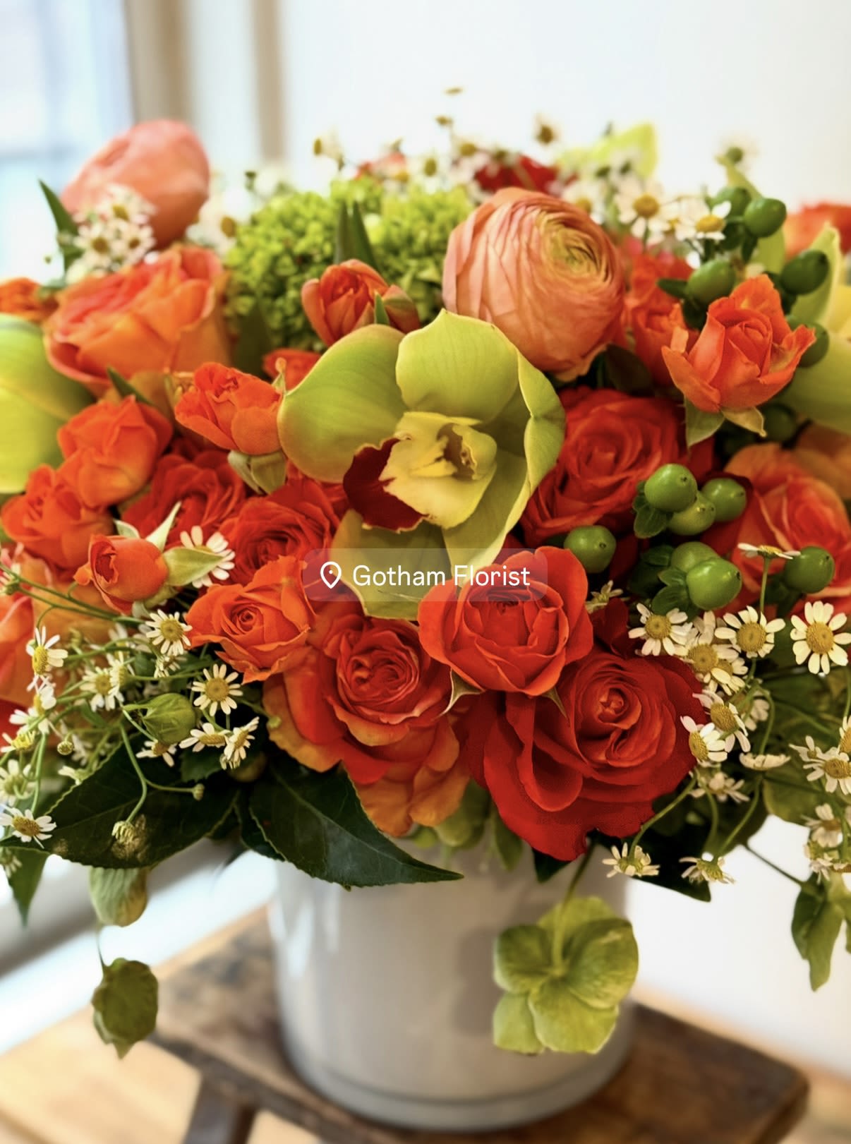 Bouquet of red and orange roses with green orchids in a white vase