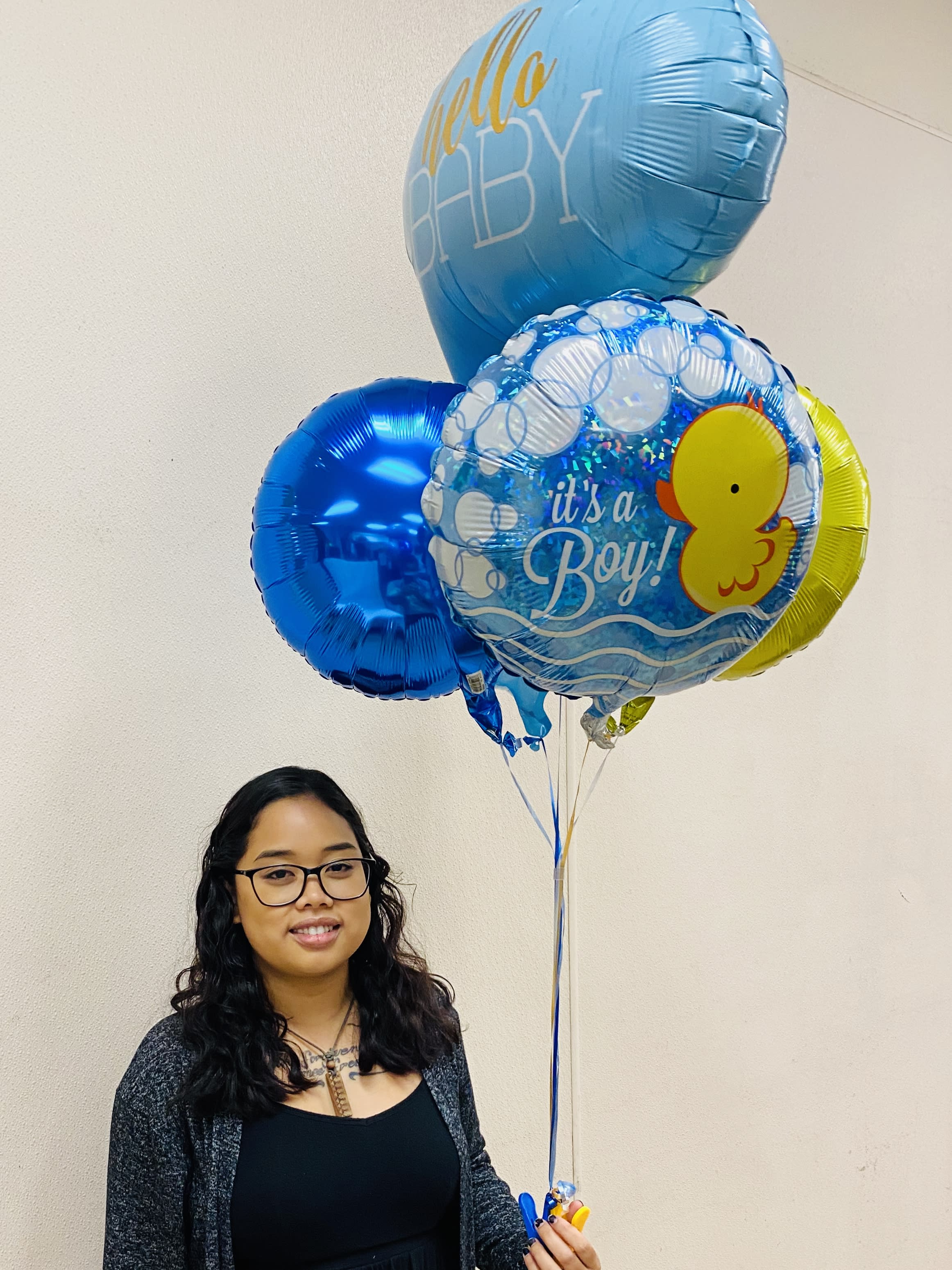Person holding a bundle of blue baby boy themed balloons with duck and hello baby text