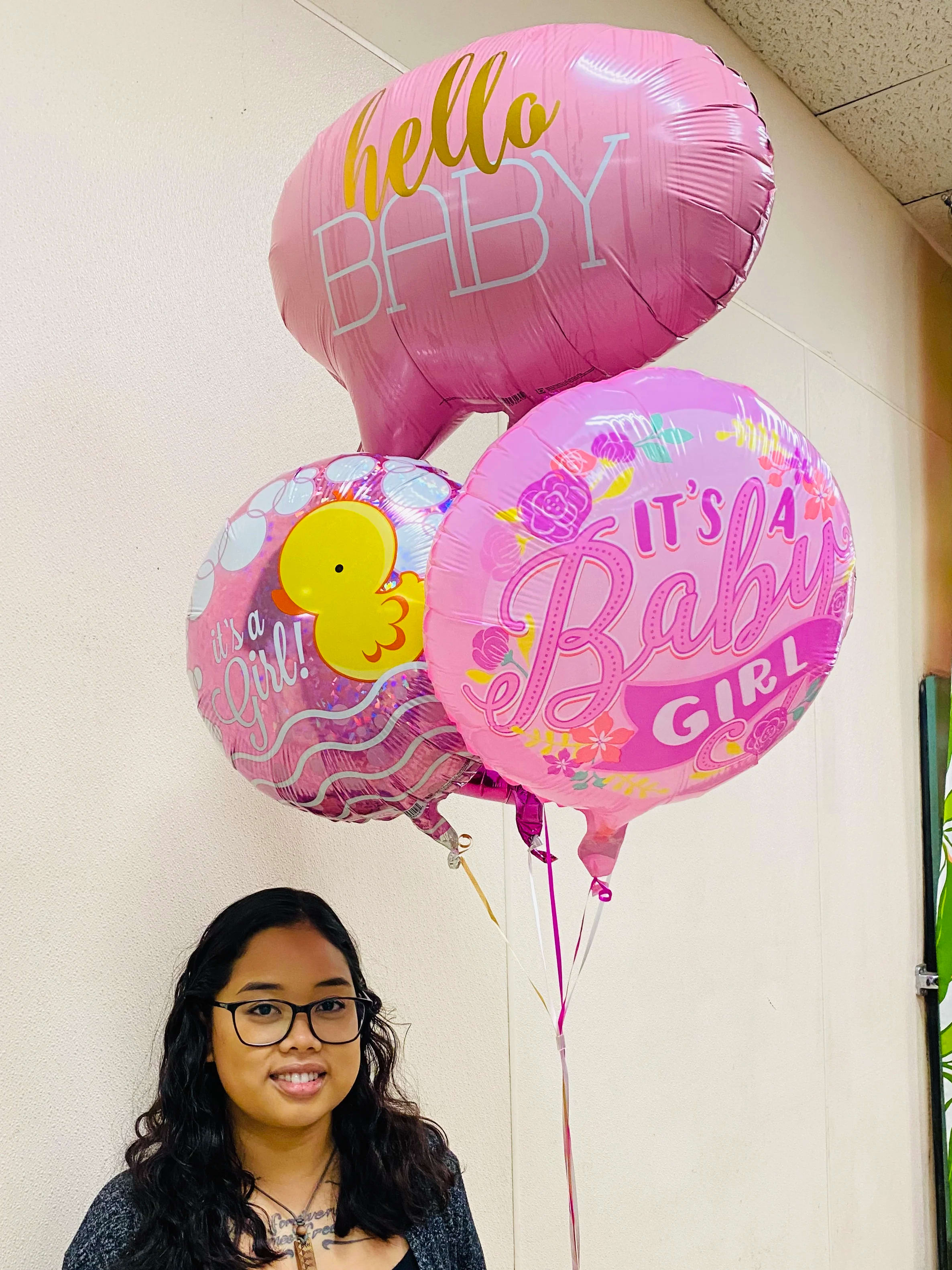 Pink baby girl themed helium balloons held by a woman indoors