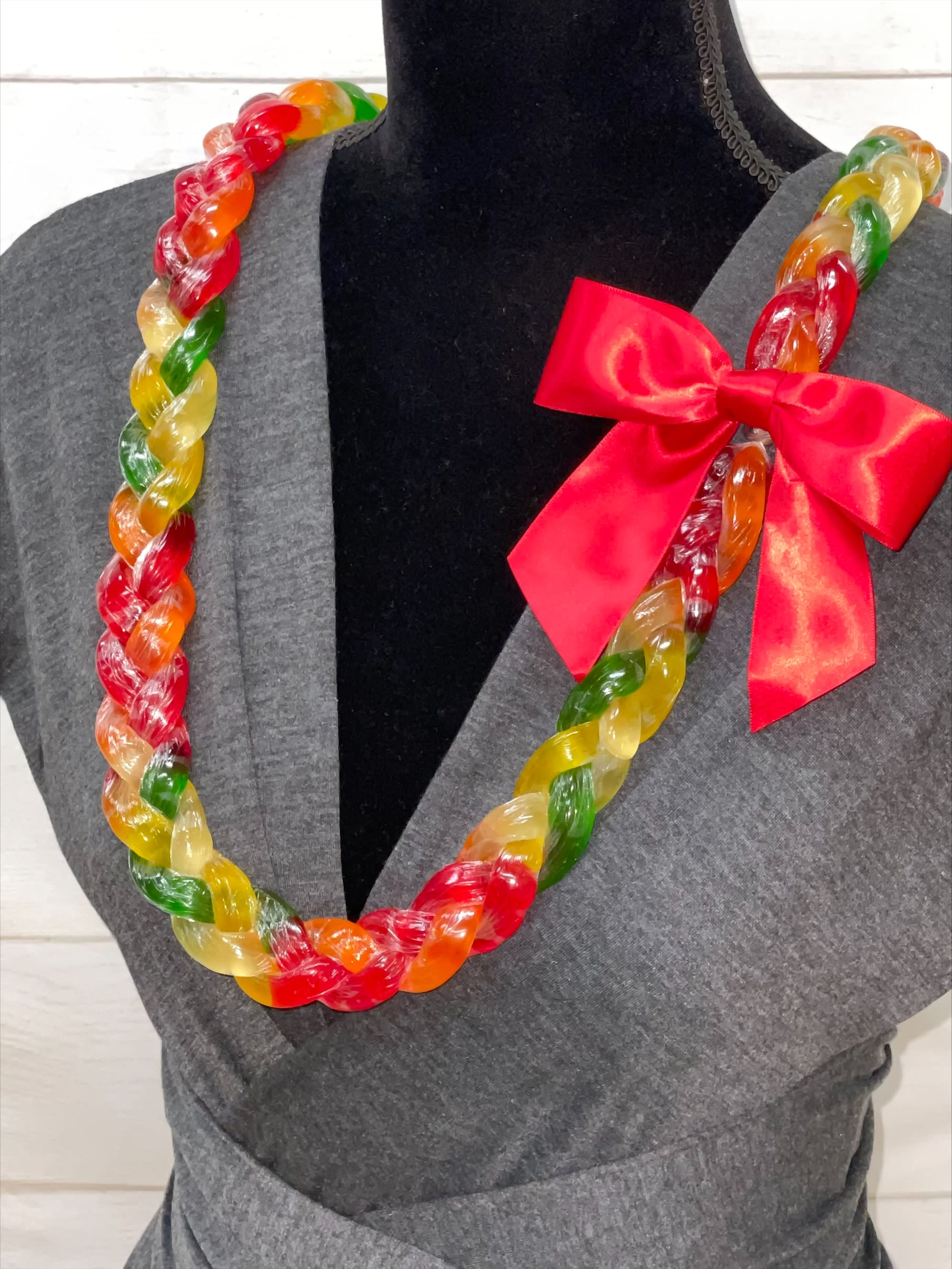 Colorful twisted candy lei necklace with red bow displayed on a gray dress form