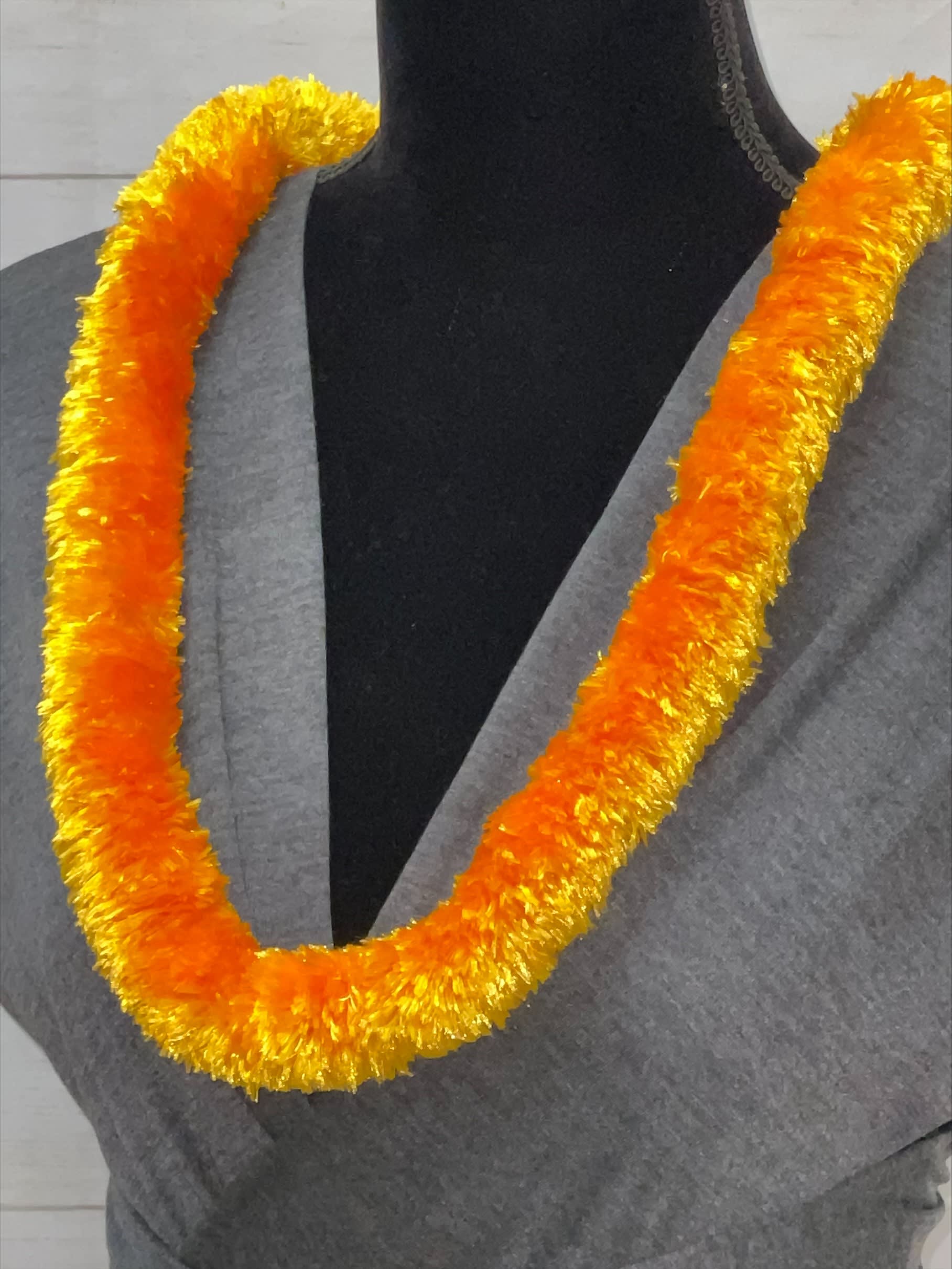 Orange and yellow fluffy lei necklace displayed on a gray-draped black mannequin.