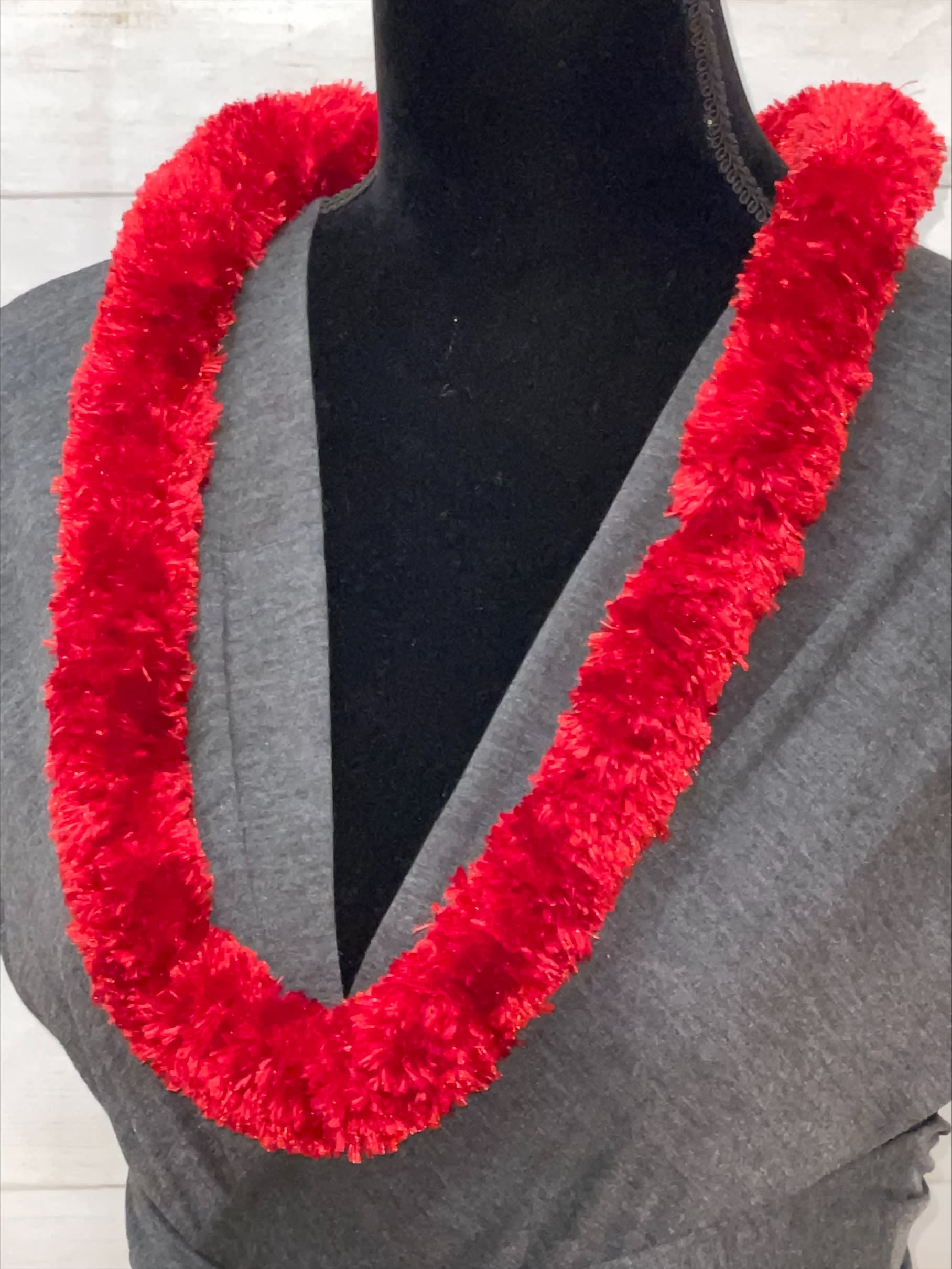 Fluffy red garland-style lei displayed on a black dress form in a gray top