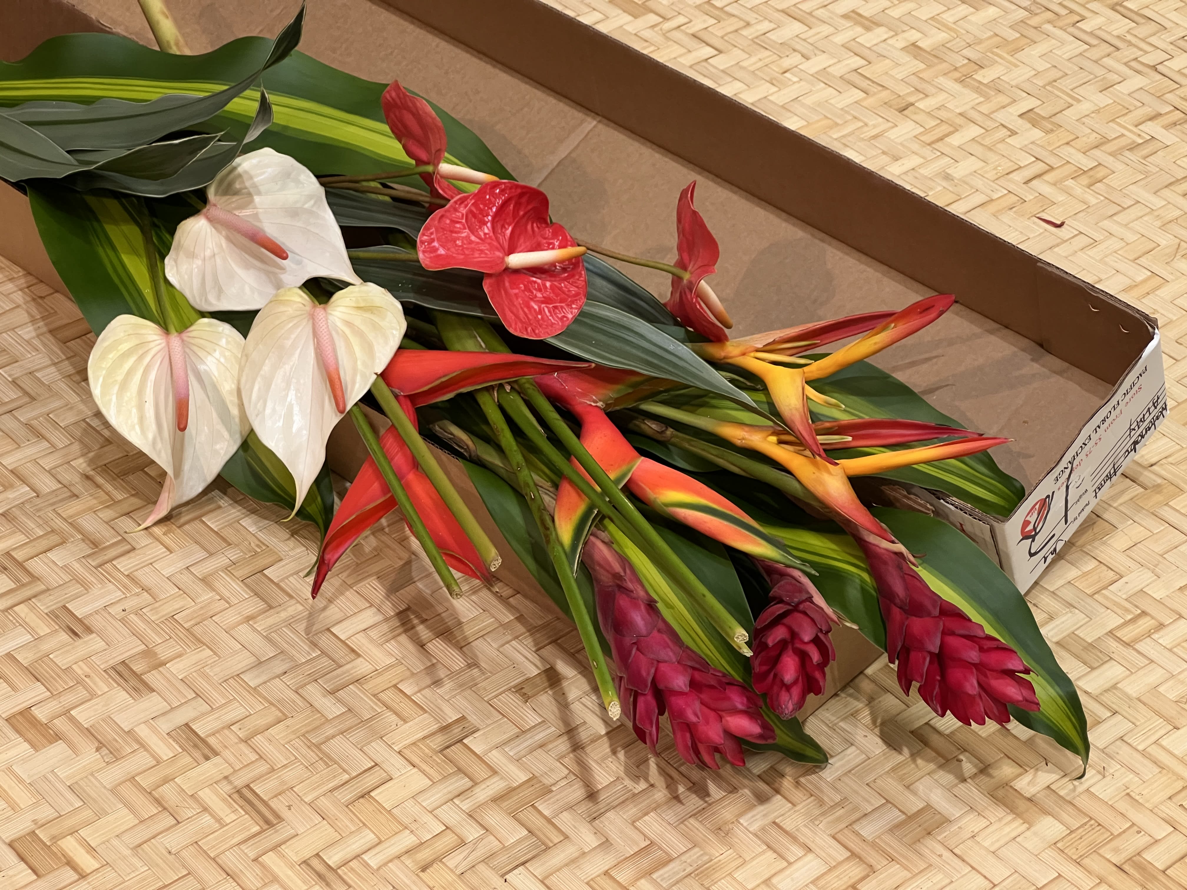 Bundle of assorted tropical flowers with large leaves laid in a cardboard box.