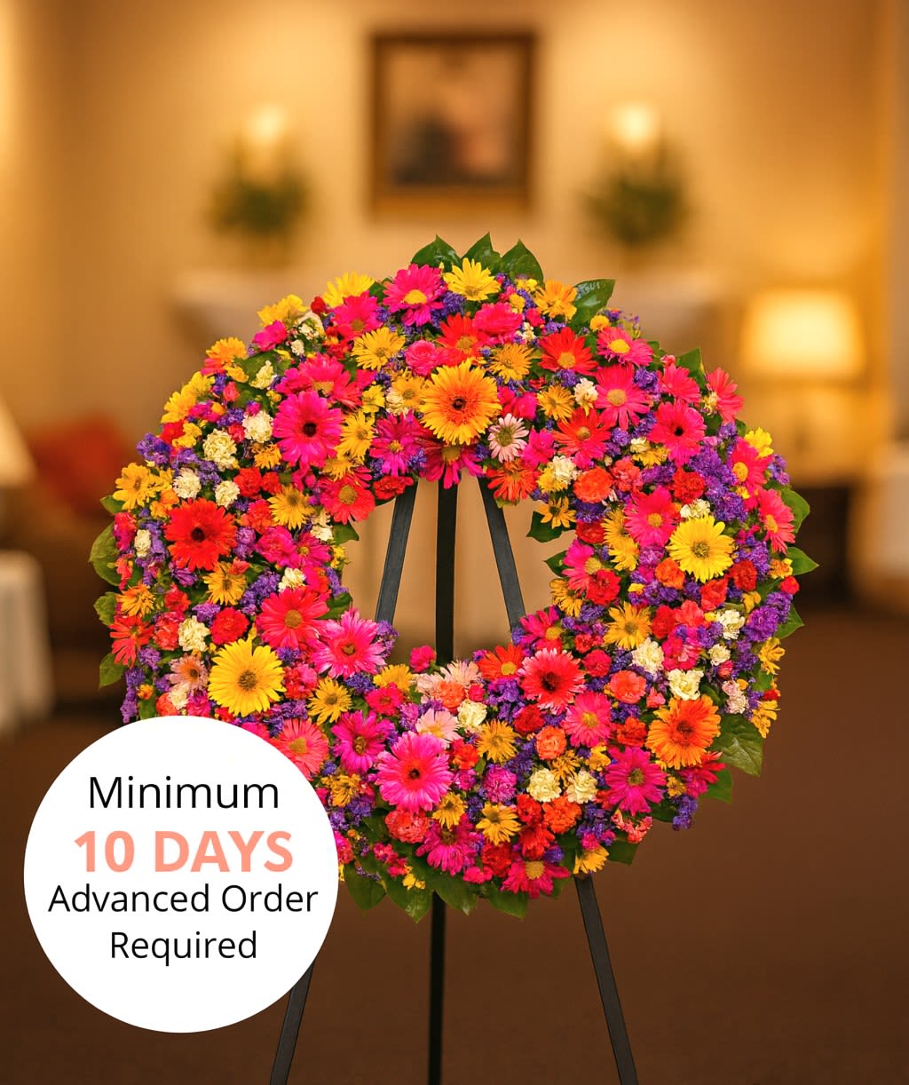 Bright circular standing wreath of mixed pink, orange, yellow, and purple flowers on a black easel indoors