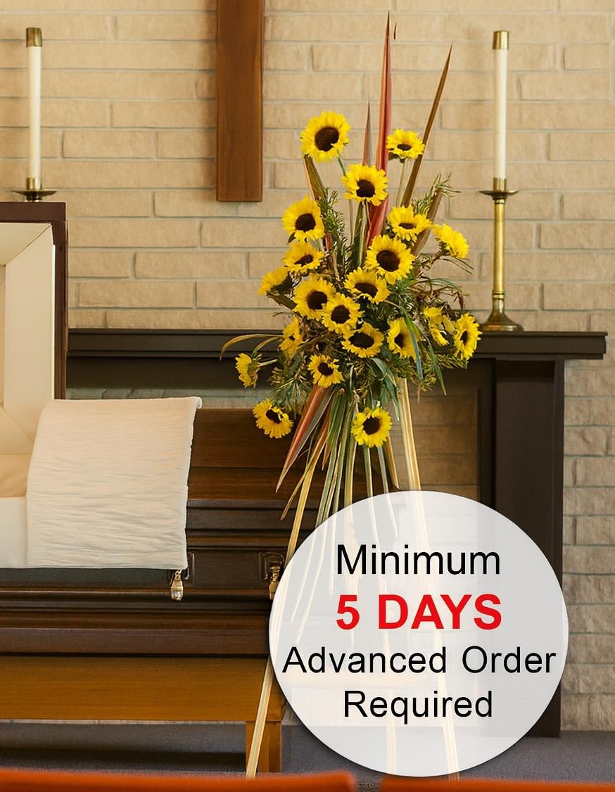 Tall easel spray of yellow sunflowers beside a wooden casket in a chapel setting